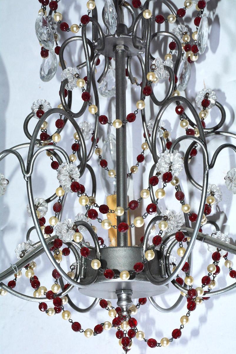 The petite vintage chandelier's armature has pewter silver tones with three lights and is embellished with pearl and faceted ruby beaded (plastic) swags attached to clear rosettes (plastic). Crystal drops. Wired for US electricity/flame bulbs. Great