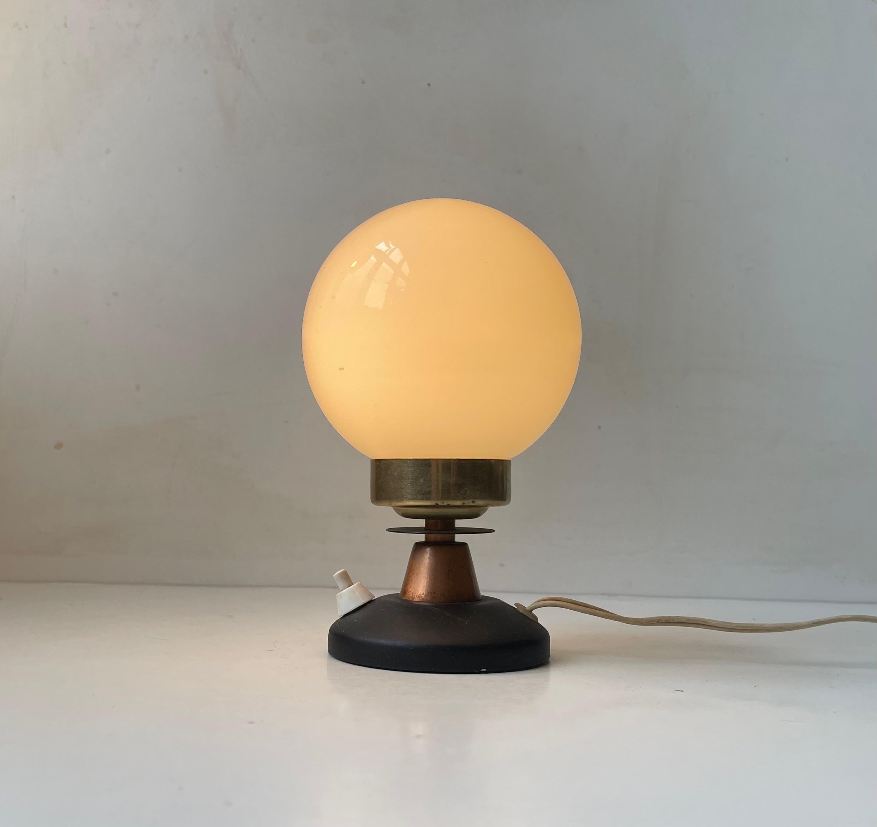 Unusual and small table lamp composed of a stylized base in copper, brass and black-painted metal. Over this configuration a floating opaline sphere in white glass. In Scandinavia we call this design a 'Space Bug' or 'Space Sphere'. It was