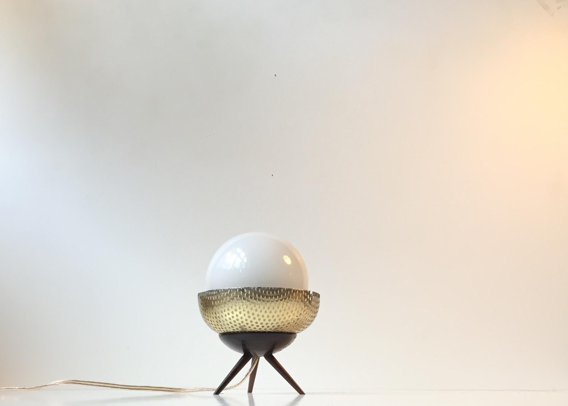 Small unusual table lamp composed of an ebony tripod base, an opaline glass sphere, and a perforated shade of brass-alloyed steel. In Scandinavia, this design is called a Space Bug or UFO. It was manufactured in Scandinavia during the 1960s.