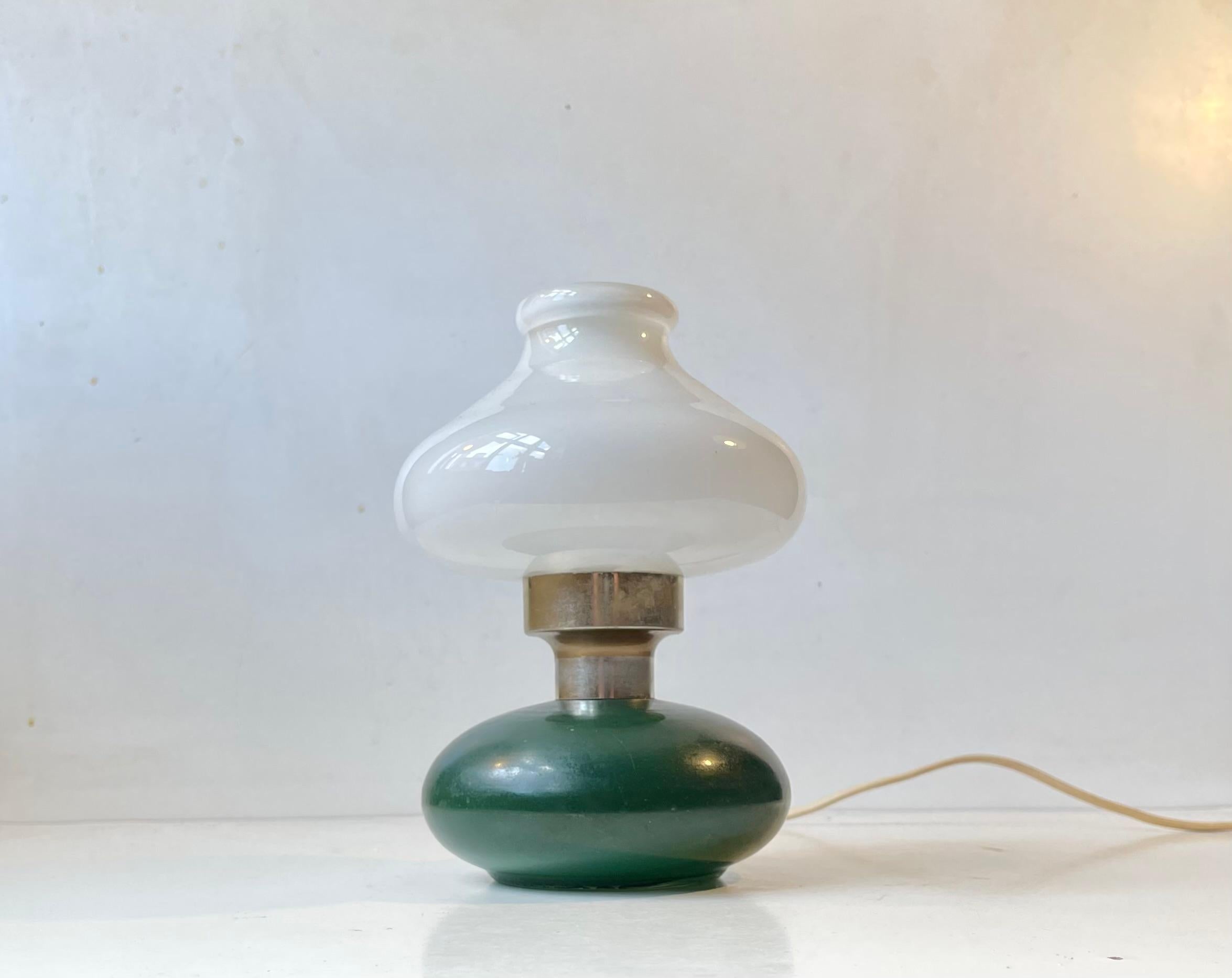 Small table light featuring a green base in painted glass and a white opaline glass, It has a switch to its cord. Manufactured in Sweden during the 1970s. Measurements: H: 20, D: 14 cm. For the US. It will come installed with a 110 watt adaptor plug
