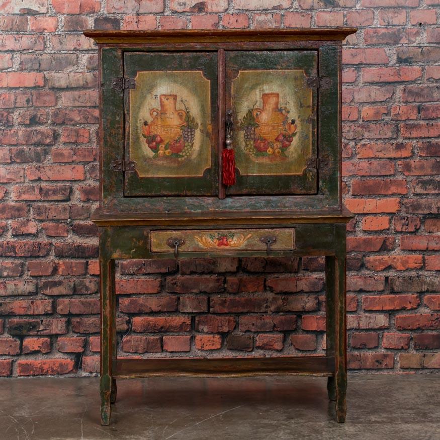 This delightful step back cabinet, while small in size, is brimming with character. Adding to its charm is the distressed painted finish featuring South American pottery and fruit on the panel doors. The interior and exterior have been given a wax