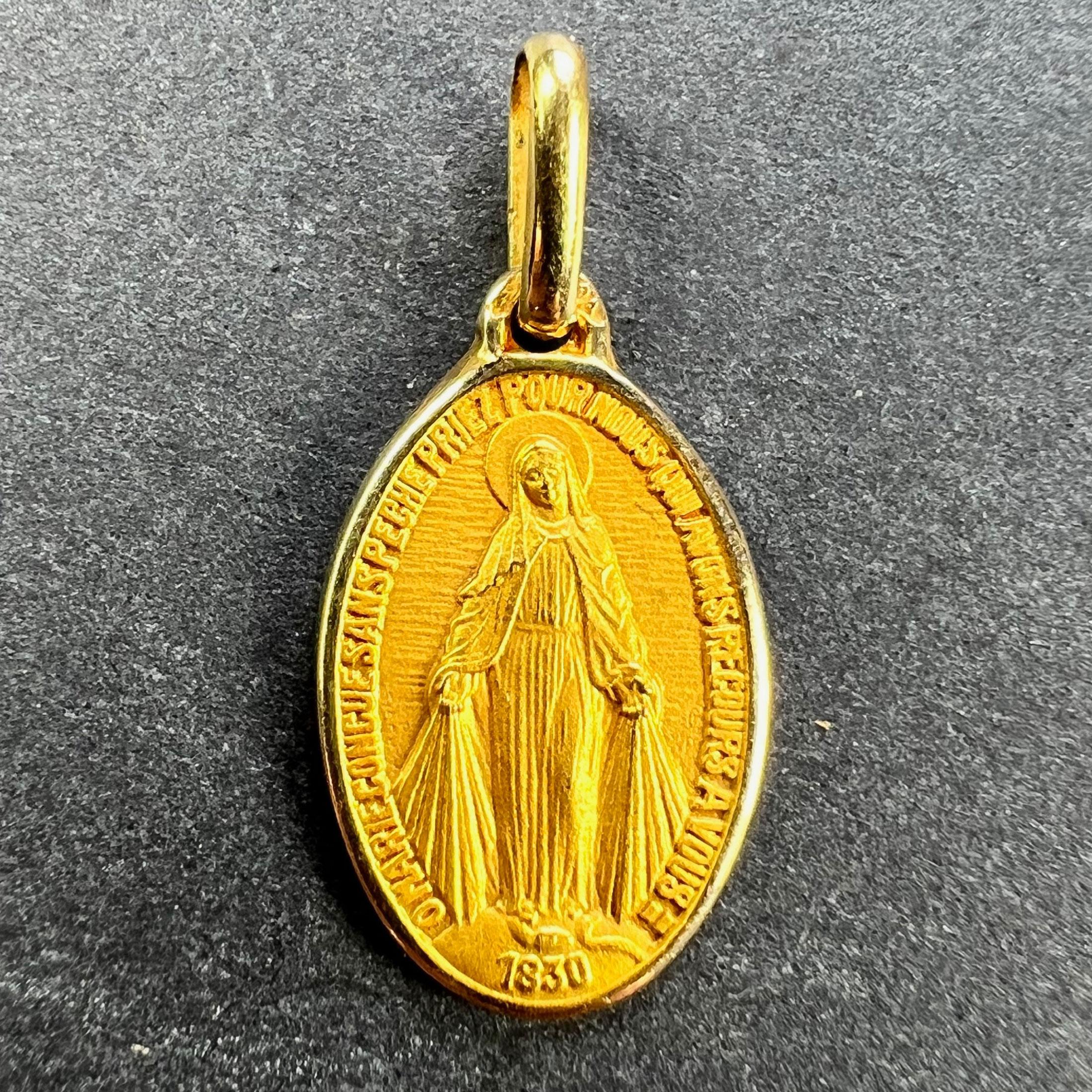 A French 18 karat (18K) yellow gold charm pendant designed as the Miraculous Medal by Augis. The medal depicts the Virgin Mary standing on a globe above the date 1830, crushing a serpent beneath her feet with rays shooting from her hands to