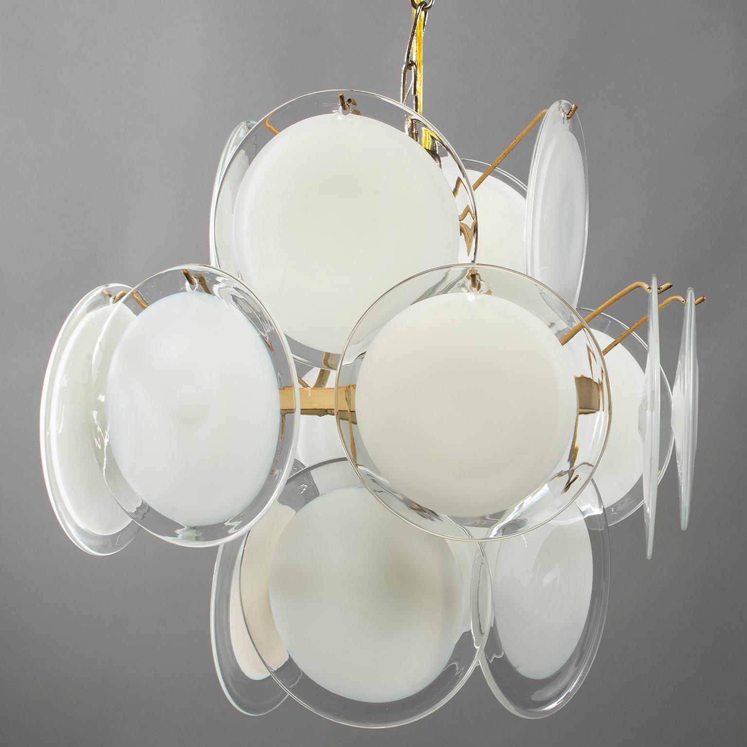 Murano glass chandelier manufactured by Vistosi features a brass plated metal base with three tiers of suspended glass disks. Round glass elements are opaque white at the centre with clear edges. Chandelier has been rewired for US electrical