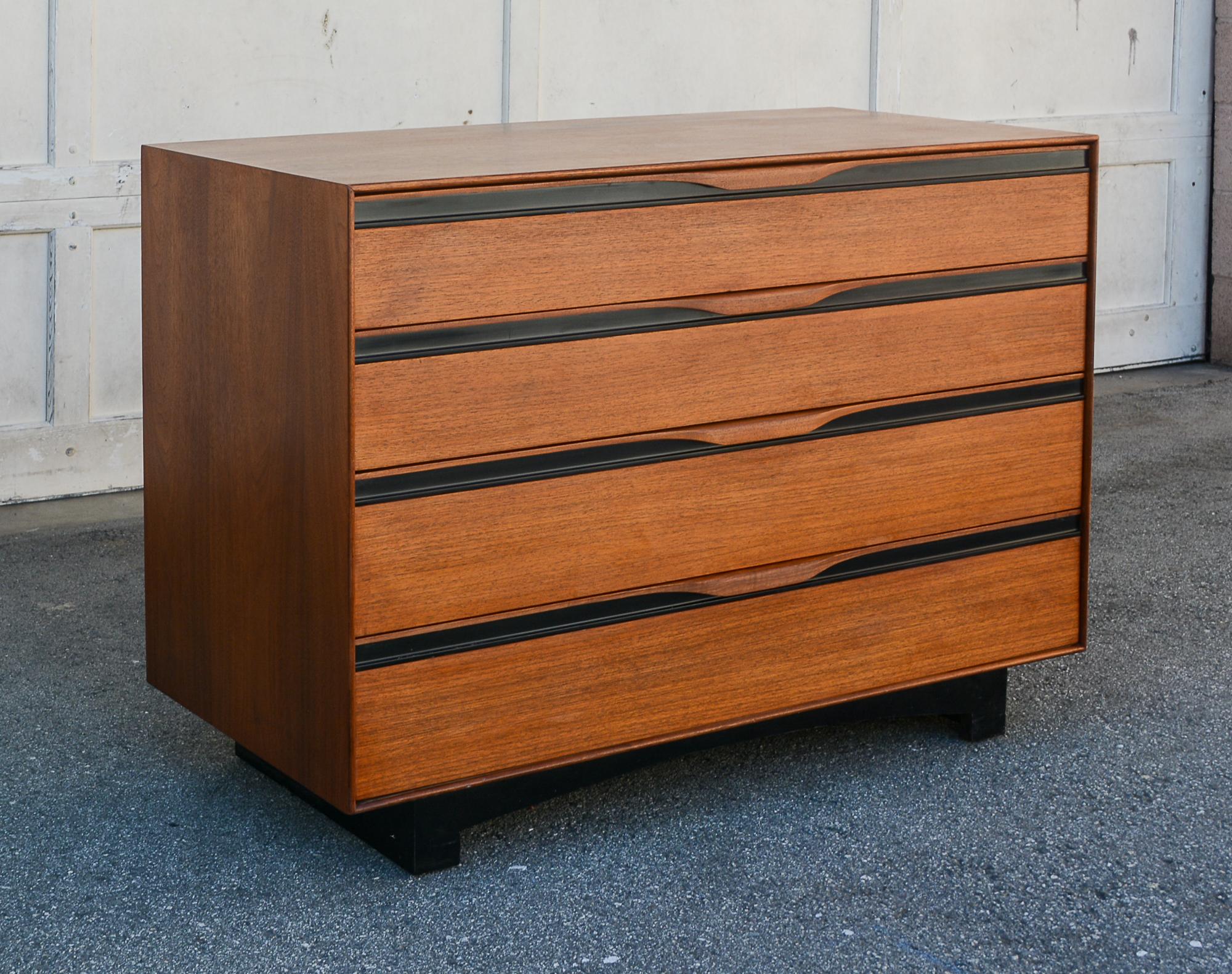 Small four drawer chest designed by John Kapel for Glenn of California. The chest is walnut with a black laminate base and black plastic strips below the drawer pulls. The drawers open and close easily on steel slides. There are movable dividers in