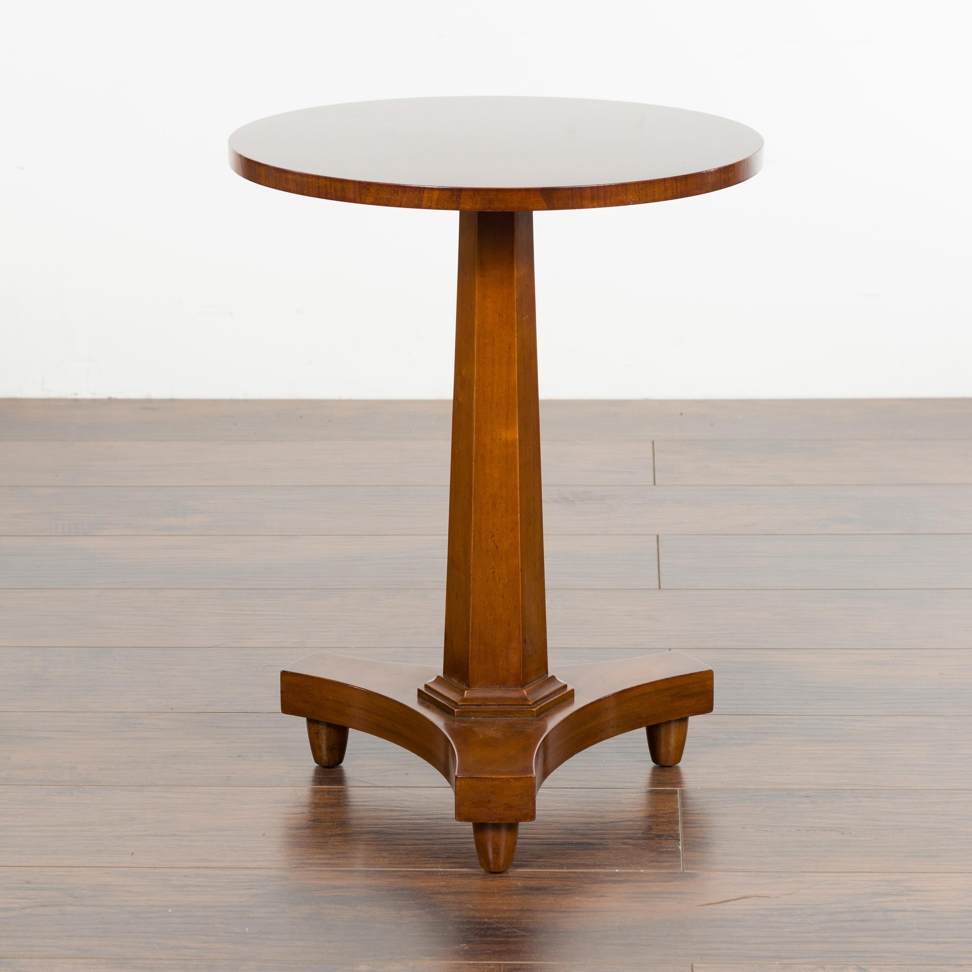 A small Baker walnut drink table from the mid 20th century, with round top and pedestal base. Made in the USA during the midcentury period, this drinks table features a circular top sitting above an hexagonal pedestal resting on an in-curving