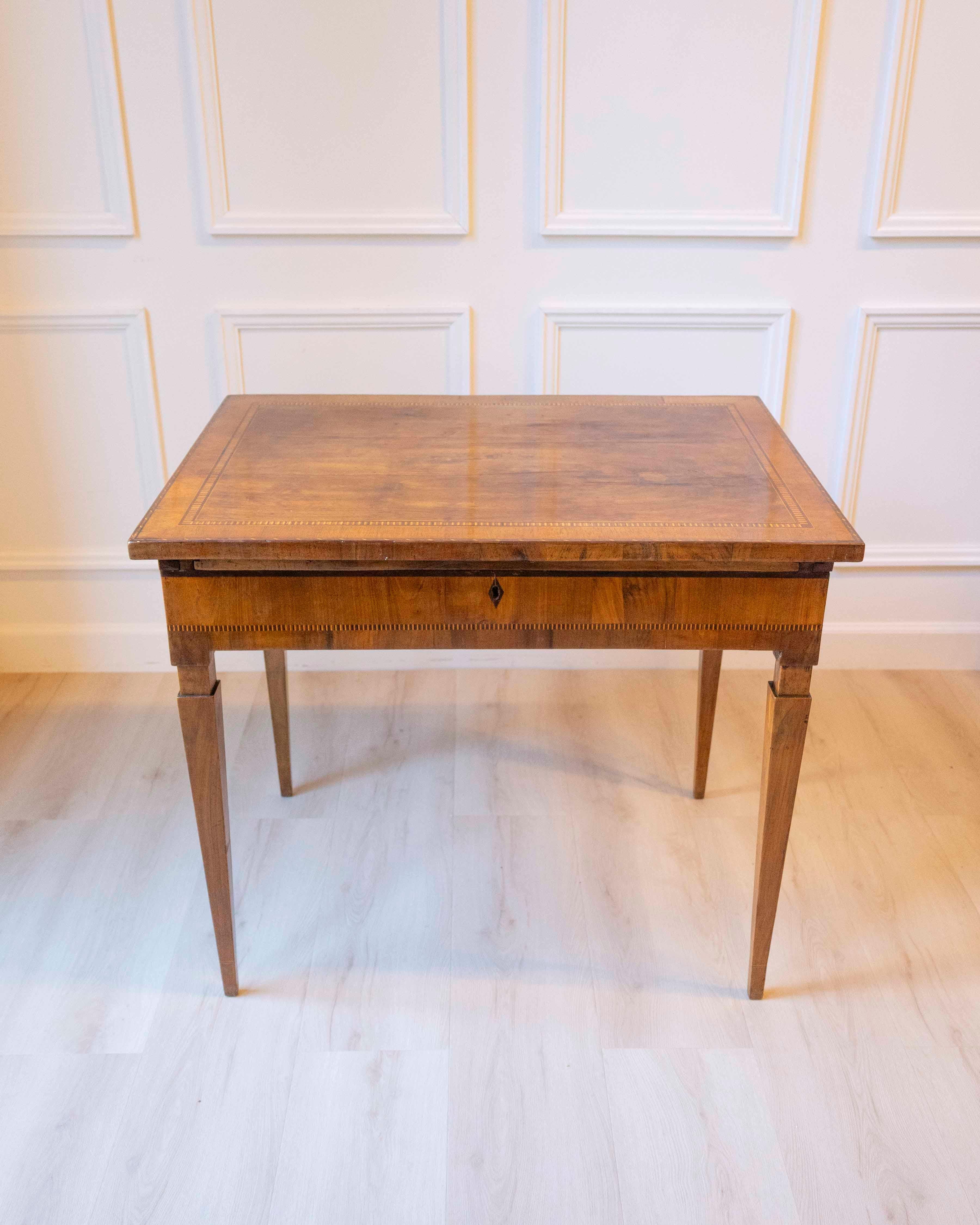 This late 18th-century Tuscan writing desk is constructed with a walnut veneer and detailed with contrasting inlaid woods that define its linear edges and emphasize its geometric clarity. The desk features a sliding upper surface that reveals a