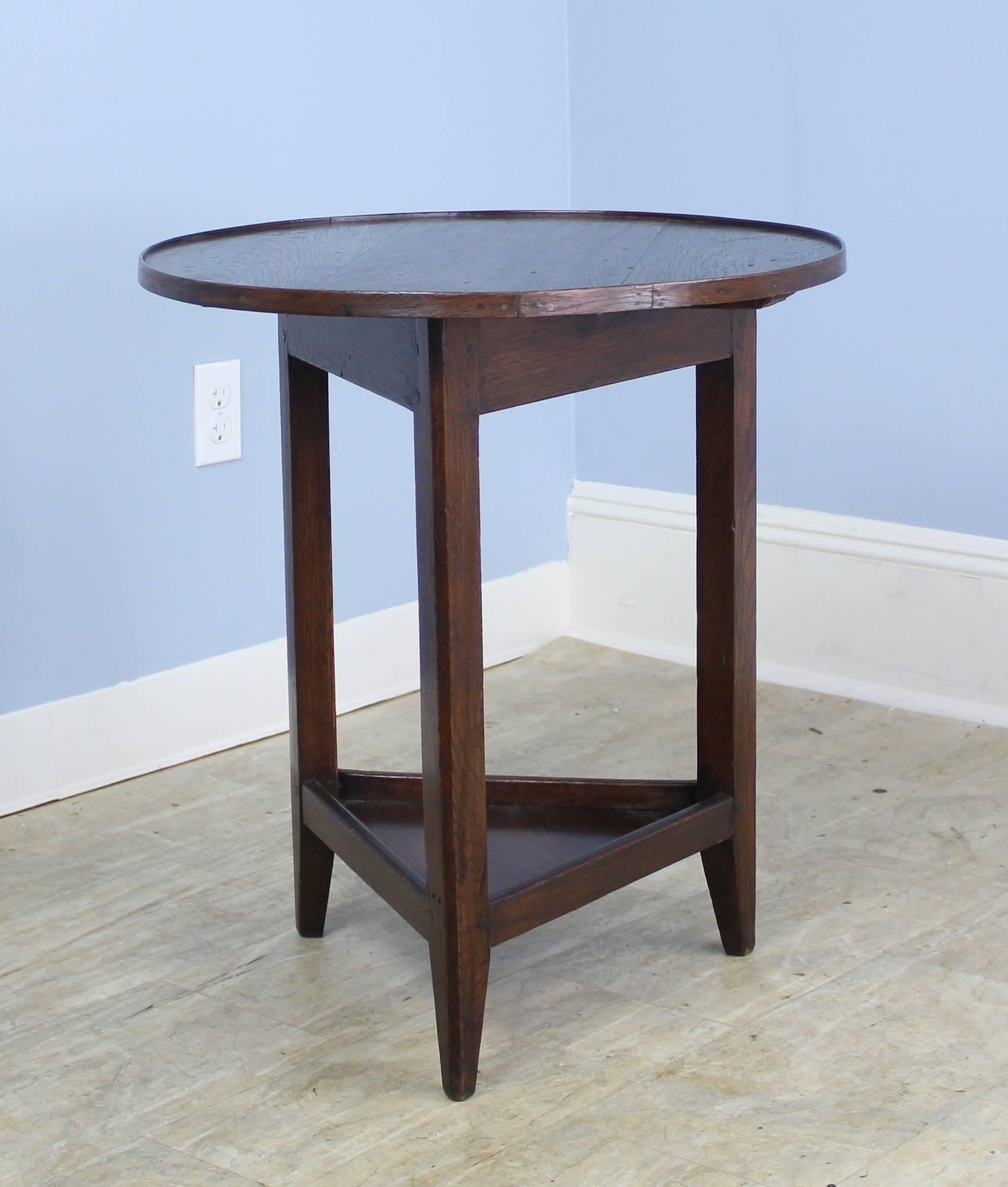 A small cricket table in rich dark oak with a lower galleried shelf. Traditional three legged base. The decorative trim around the top and the tapered feet add an additional design note.