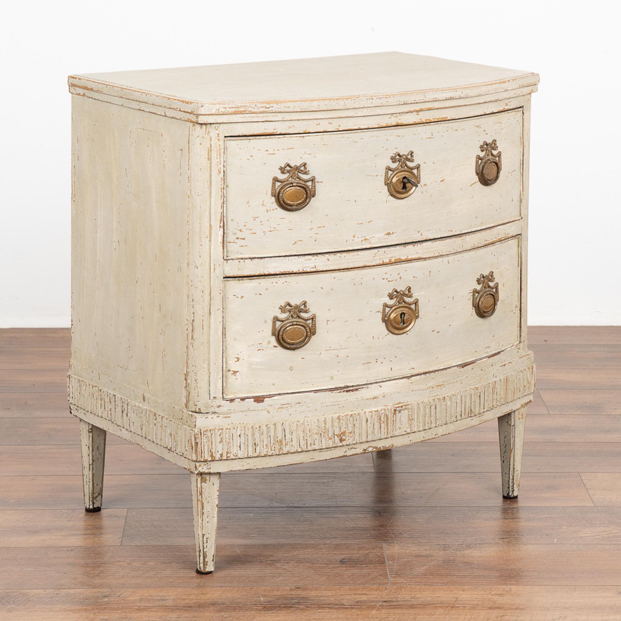 This small chest of drawers is quite dramatic thanks to the bow front and fluted carving along the skirt. Rests on tapered feet.
Restored, later professionally painted in layered shades of white and lightly distressed to fit the age and grace of