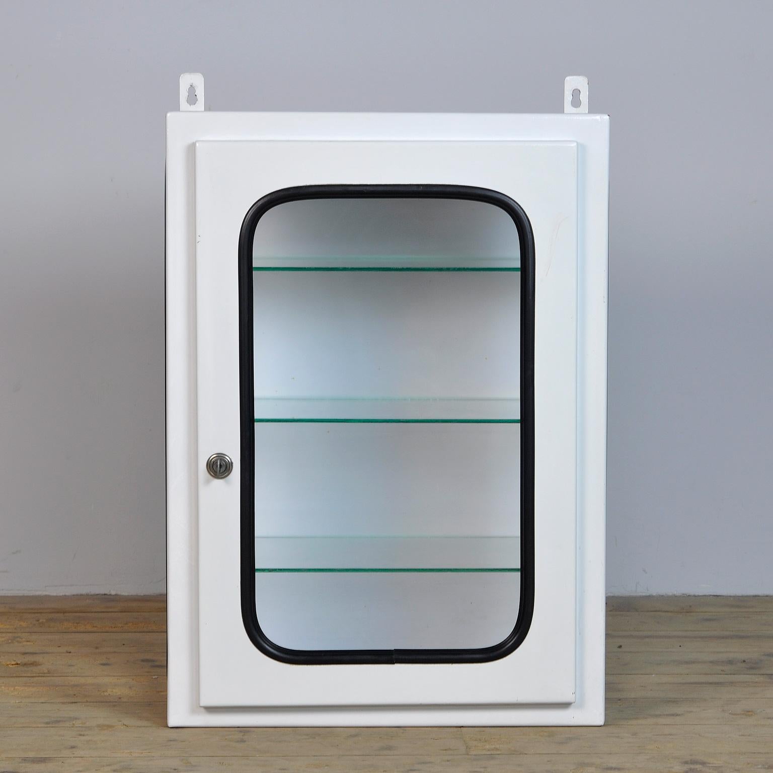 This medicine cabinet was designed in the 1970s and produced circa 1975 in Hungary. It is made of iron and glass and is held by a black rubber strip. The cabinet comes with three adjustable glass shelves.