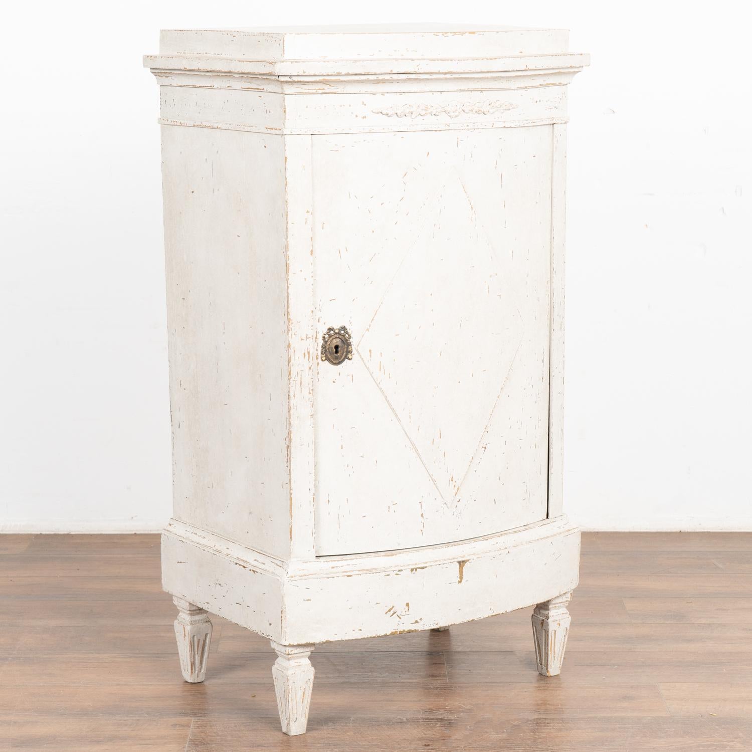 Lovely Swedish country white painted bow front small cabinet standing on fluted tapered feet.
Traditional diamond motif on single panel door which opens to reveal two internal shelves.
Newer professionally applied antique white painted finish gently