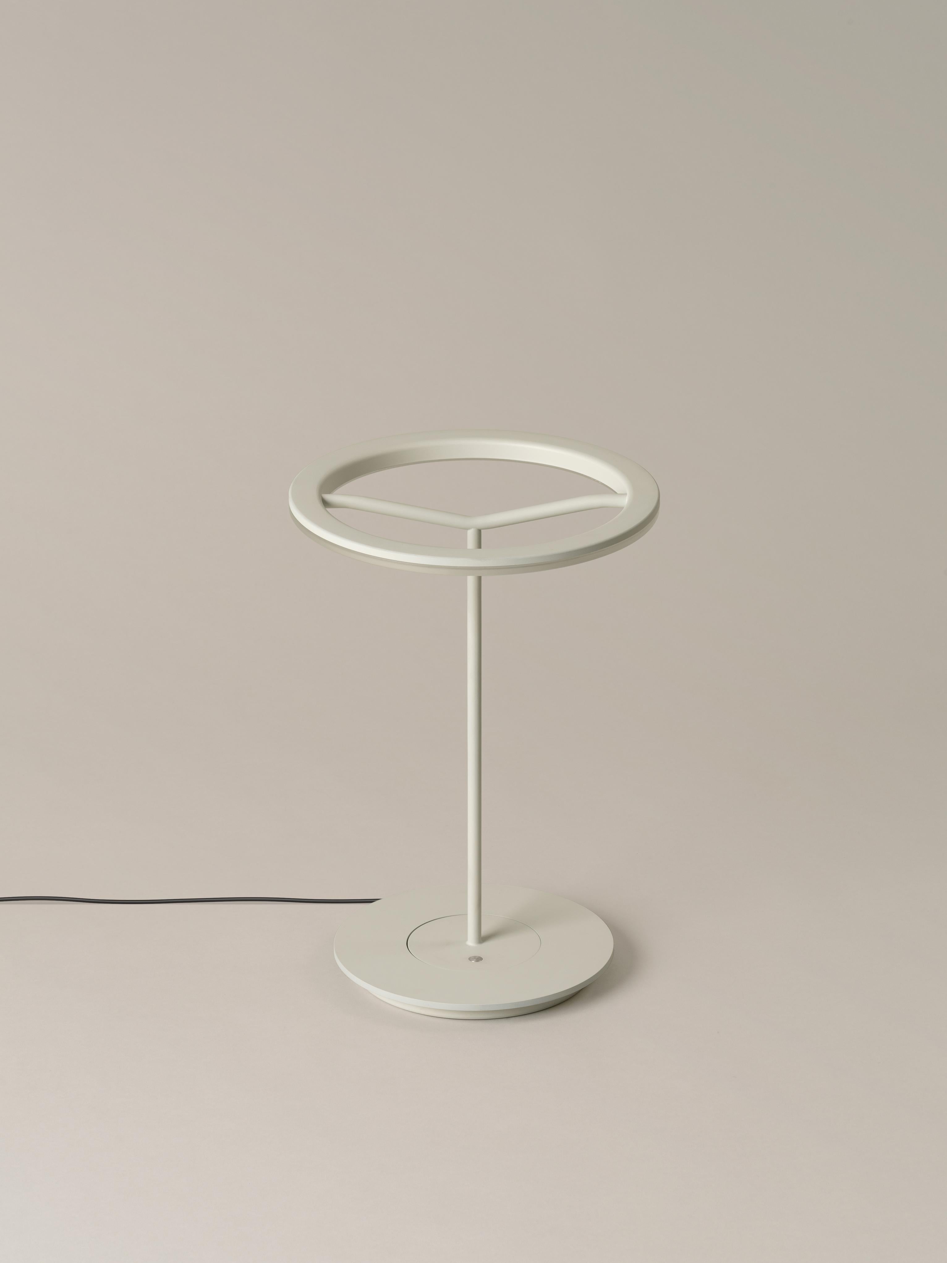 Small white sin table lamp by Antoni Arola.
Dimensions: D 25 x H 36 cm.
Materials: Metal.
Available in white or graphite, with or without shade.

A lamp that combines simplicity and technology to create a lucent ring of light suspended in the