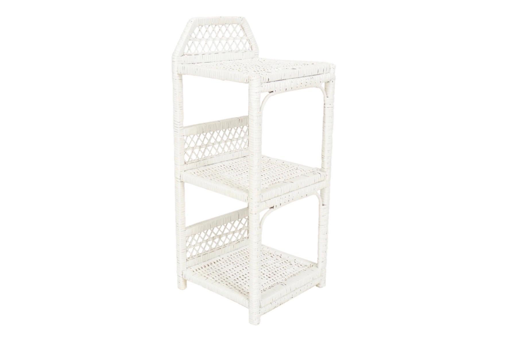 A small woven wicker étagère with three shelves in white. Each shelf has a back rail decorated with an open lattice weave.