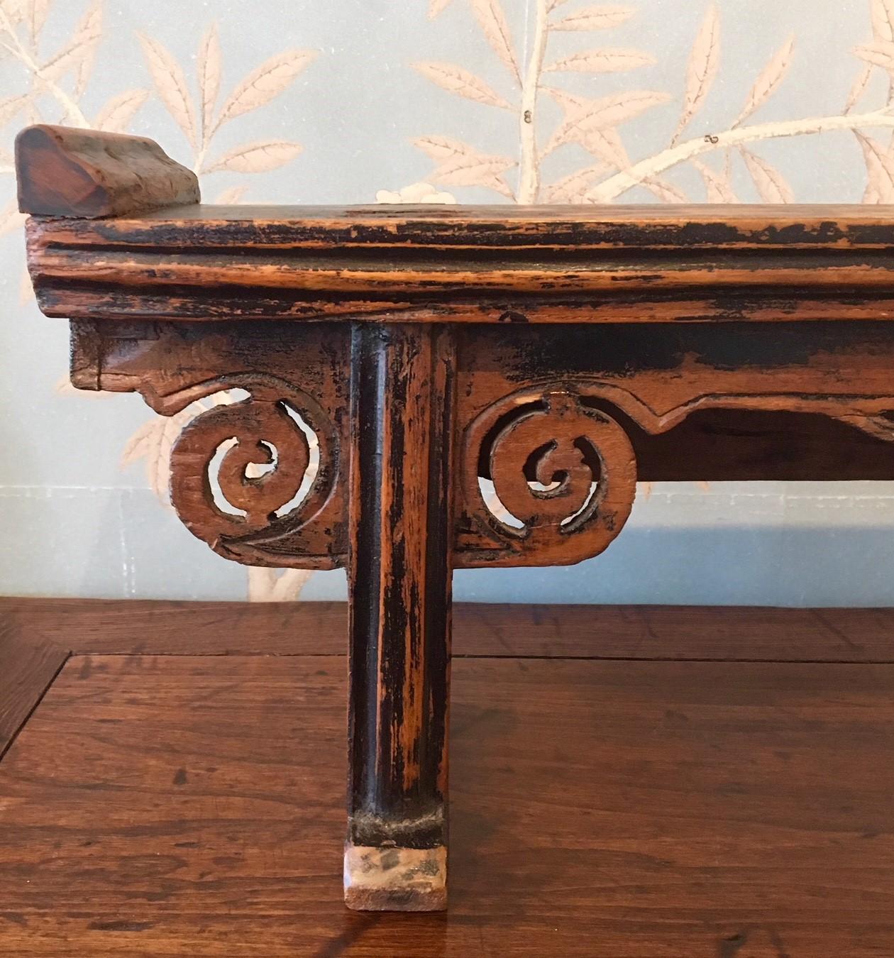 A small mid-19th century wooden altar table with worn black lacquer finish, cloud spandrels at tops of legs, and decorative apron.