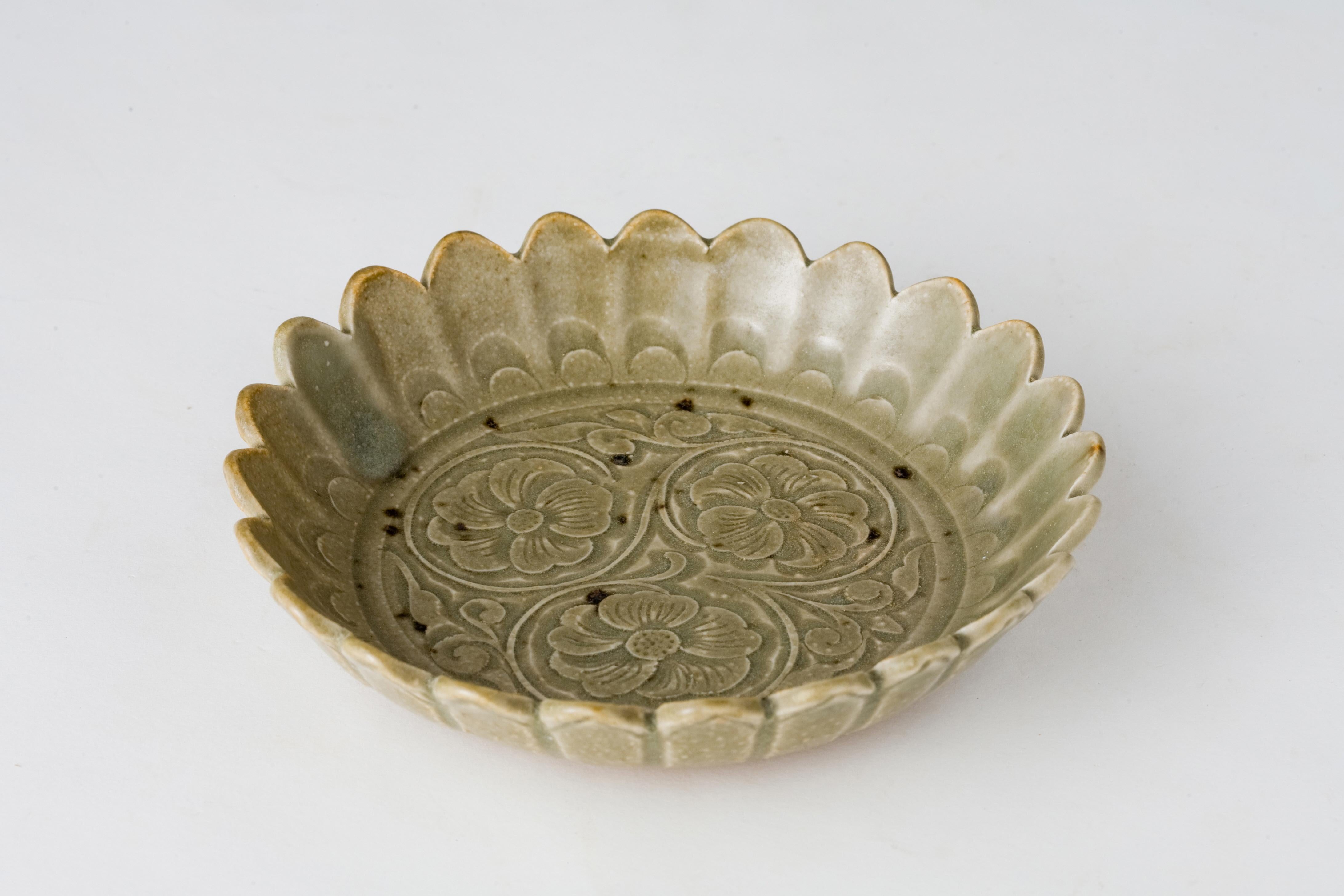 Potted with the fluted sides rising from a recessed base, carved to the interior with Chrysanthemum, covered overall with a grayish-green glaze, save for a ring to the underside left unglazed to reveal the gray stoneware body

Period : Jin