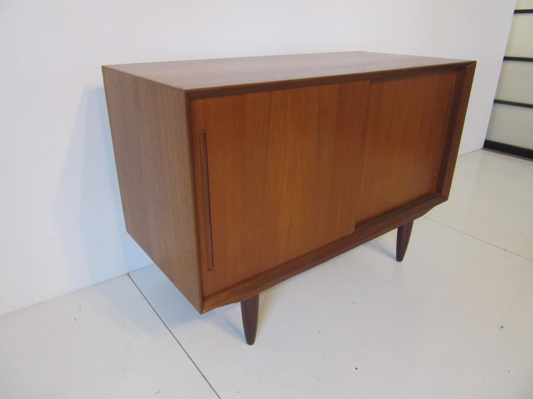 A smaller scale teak wood credenza with two sliding doors and without a shelve , can be used for your media cabinet , marked to the bottom made in Denmark.