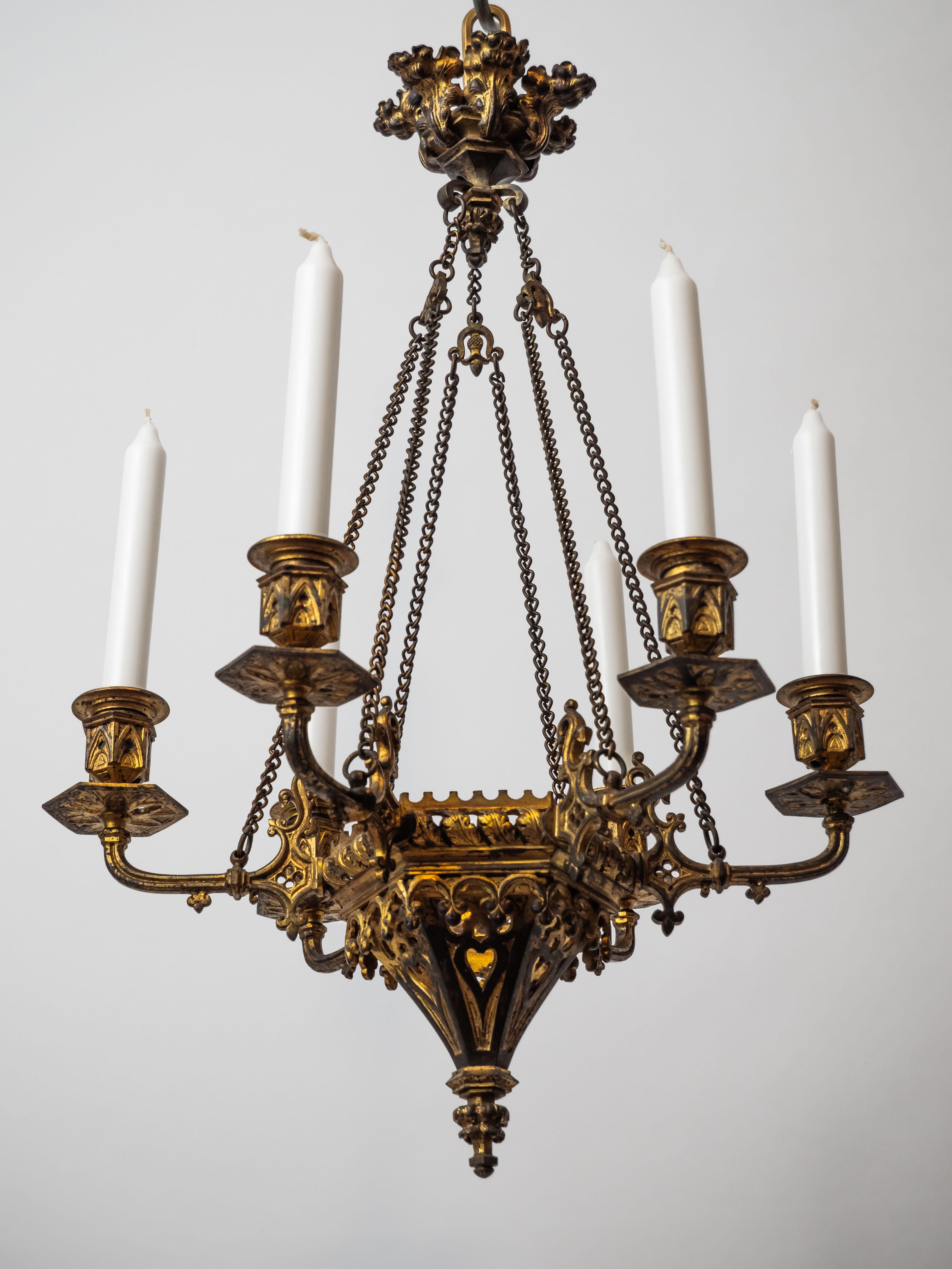 This Neo-Gothic six-armed candle chandelier is a wonderful example of historic design. The chandelier is made of bronze and is decorated with a golden patina that gives it an antique look. The entire chandelier is richly decorated with Gothic