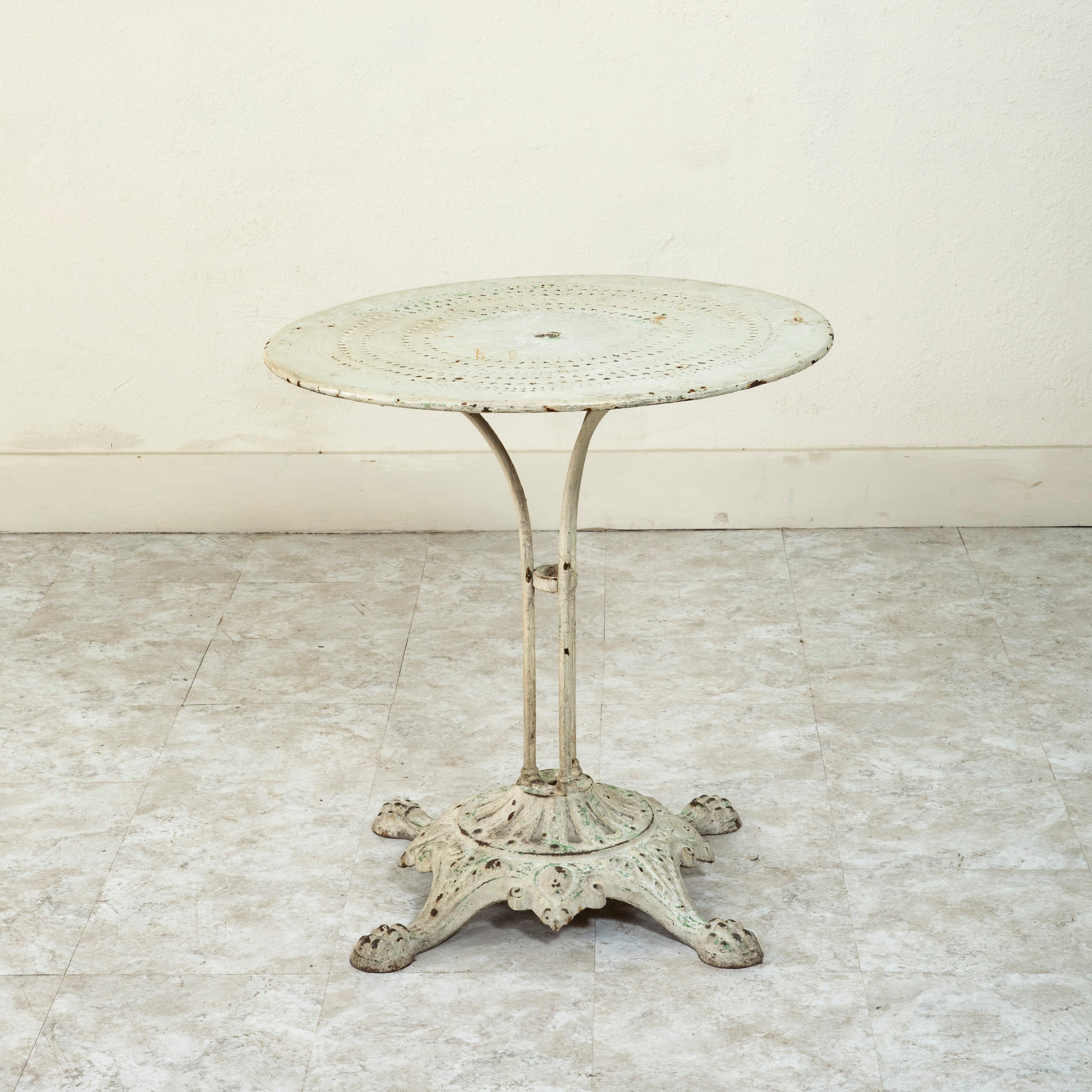 This French iron garden table from the late nineteenth century features a pierced metal top with a hole in the middle for an umbrella on a cast iron base. The top is supported by four iron rods mounted on an iron pedestal base. The pierced cast iron