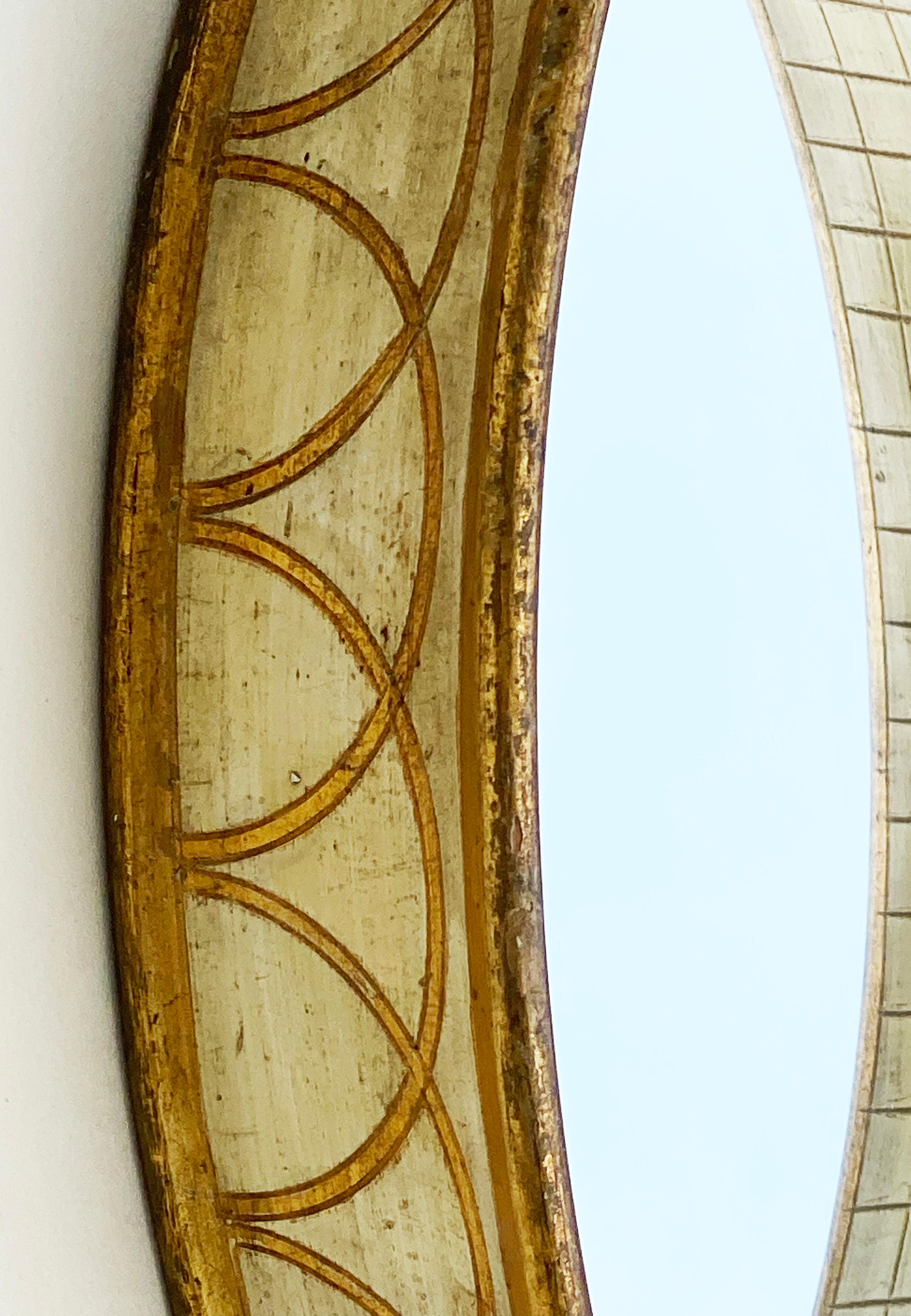 Here is a lovely smaller-scaled oval Florentine mirror in ivory and gold. It has a dramatic deep profile that flares out--creating a shadowbox effect. There is a label on the verso stating the mirror is made in Italy. There's also a small hook for