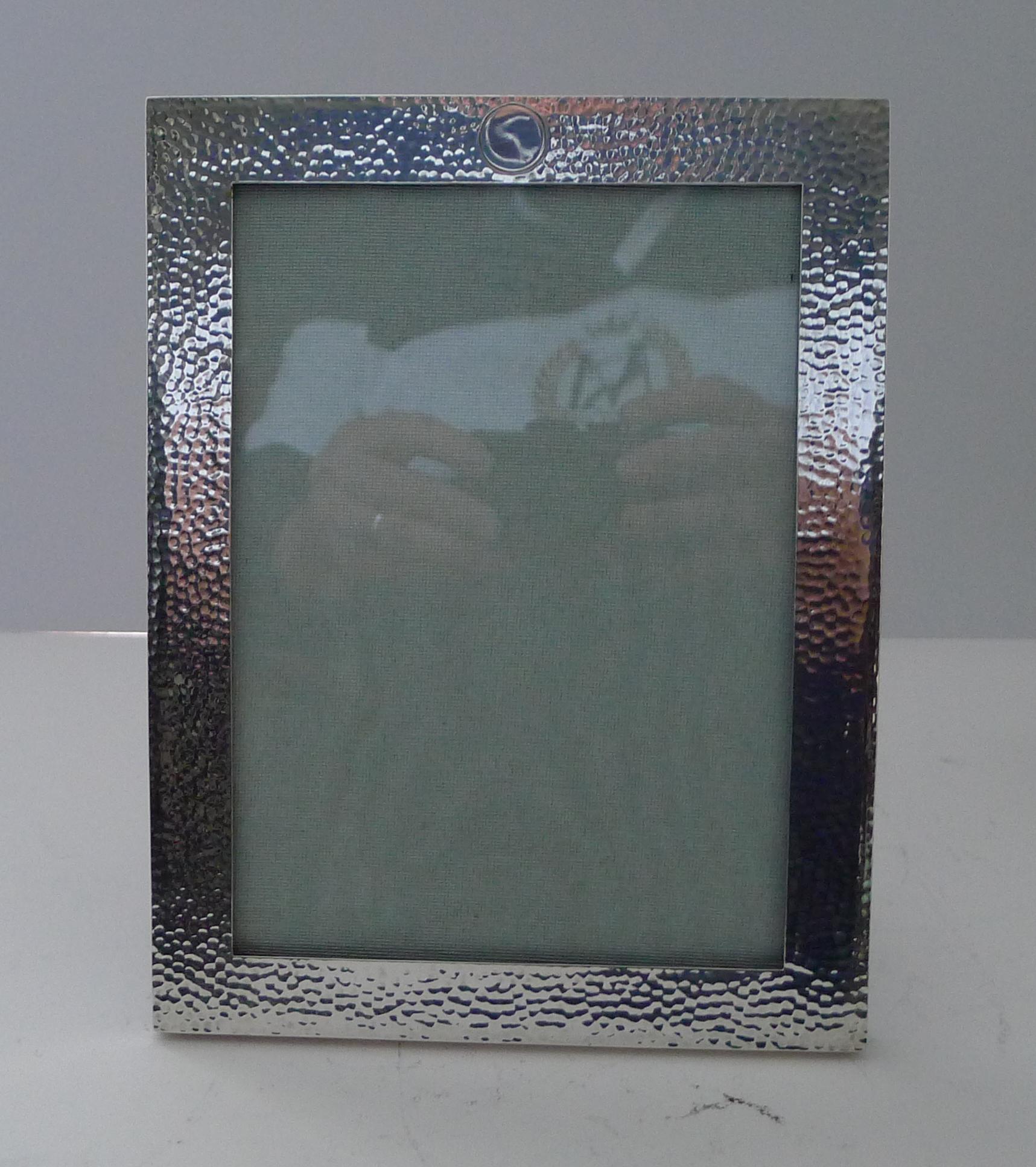 A very smart photograph frame made from English solid / sterling silver affixed to a solid English Oak backing which incorporates a folding easel stand.

The silver has a hand-planished finish, popular today as it fits in to almost any interior