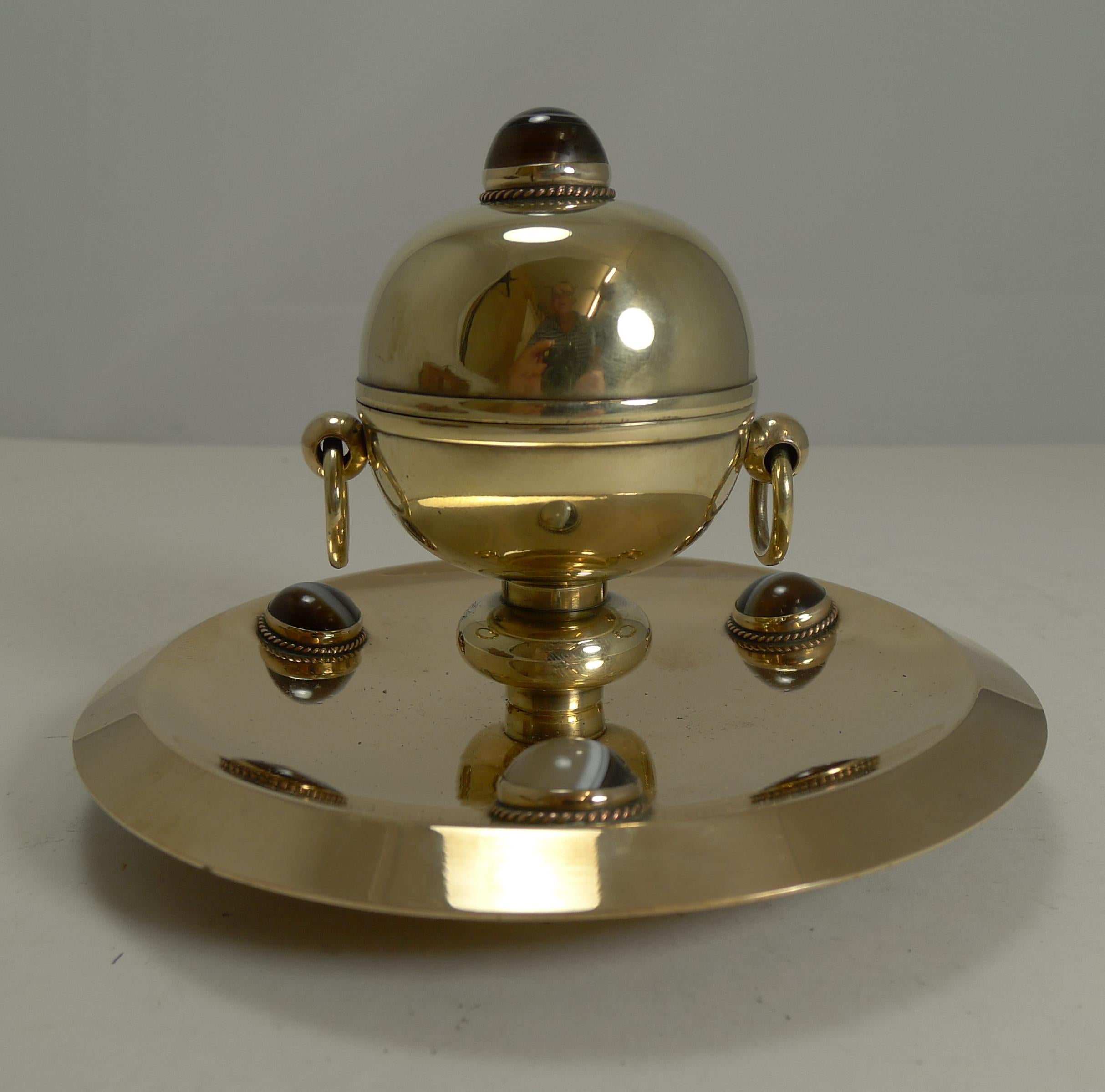 A handsome Victorian English inkwell made from a combination of polished bronze (base) and brass (spherical inkwell). The metals have been professionally polished to gleam showcasing the four polished cabochon agate stones. There is a ring handle to