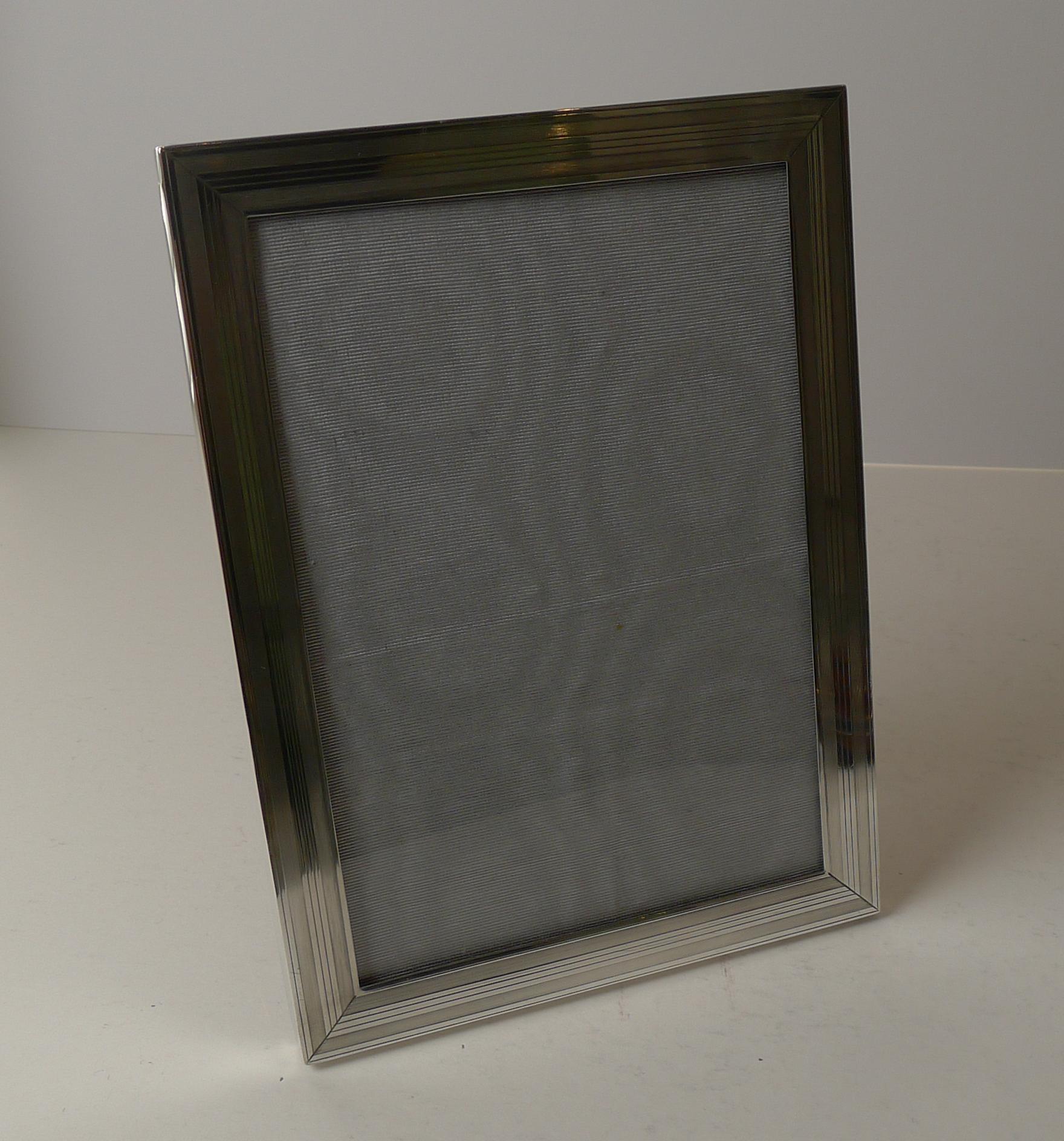 A terrific and very smart photograph frame made from English sterling silver beautifully decorated with a linear engine turned decoration.

The back is made from solid English Oak with a folding easel stand.

The silver is fully hallmarked for