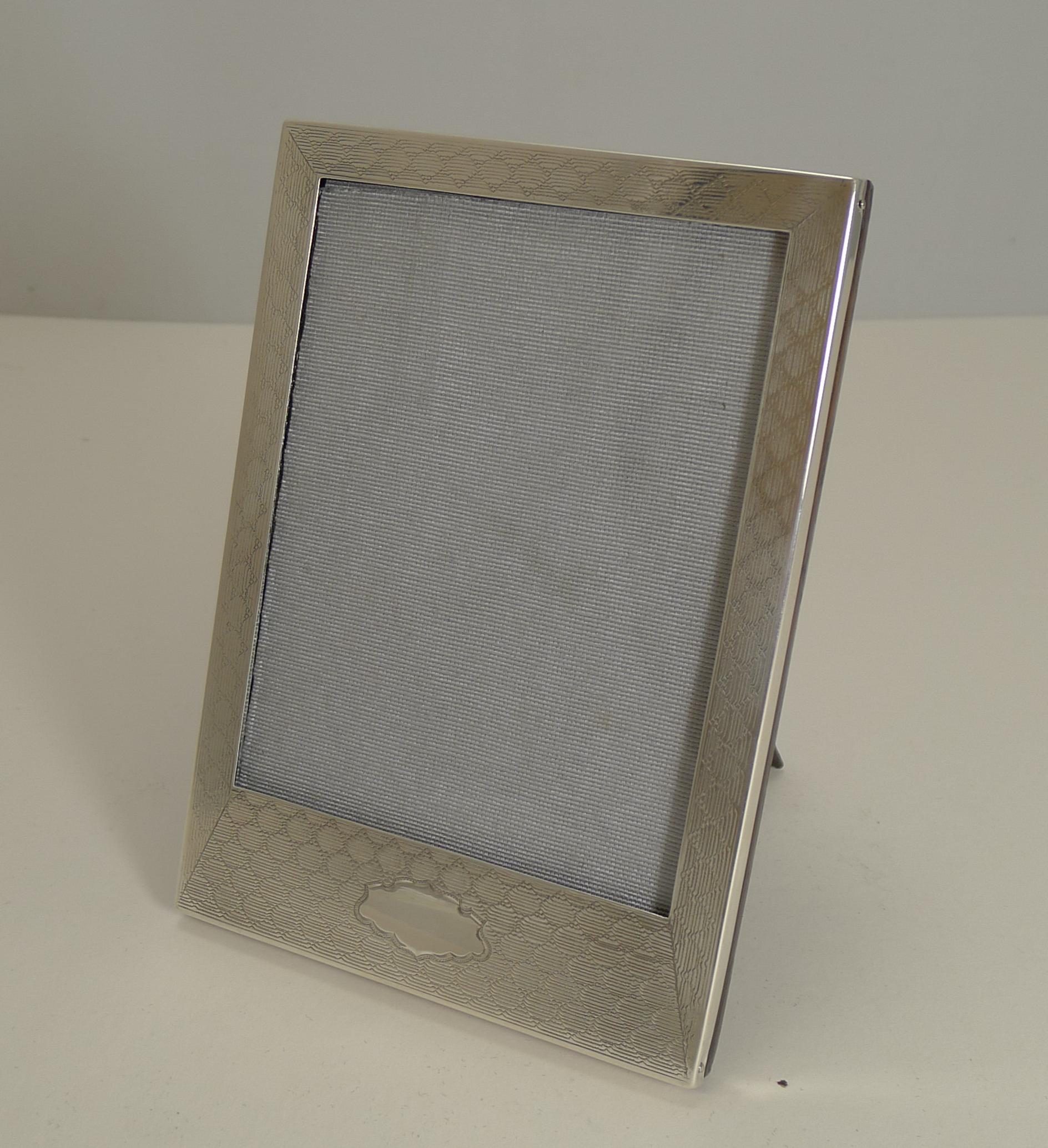 A very smart and elegant photo frame made from English sterling silver with a magnificent engine turned decoration incorporating a shaped vacant cartouche at the bottom.

The back is made from solid English oak, with a folding easel stand. The