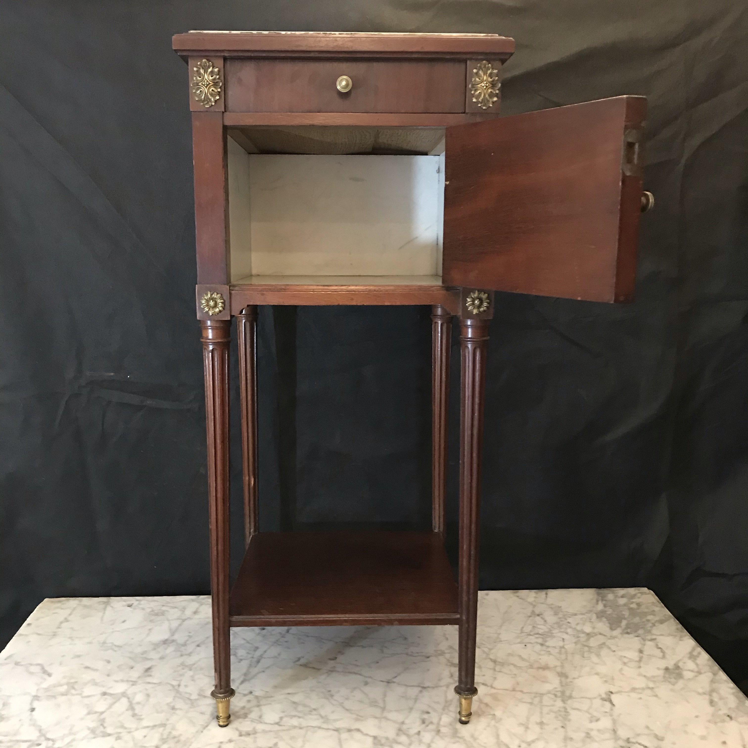 A smart Louis XVI walnut nightstand cabinet or end table with Carrara marble top and interior having a drawer for storage and lower shelf. The cabinet body has squared corners with gilded fluting and solid sides. The drawer and cabinet have