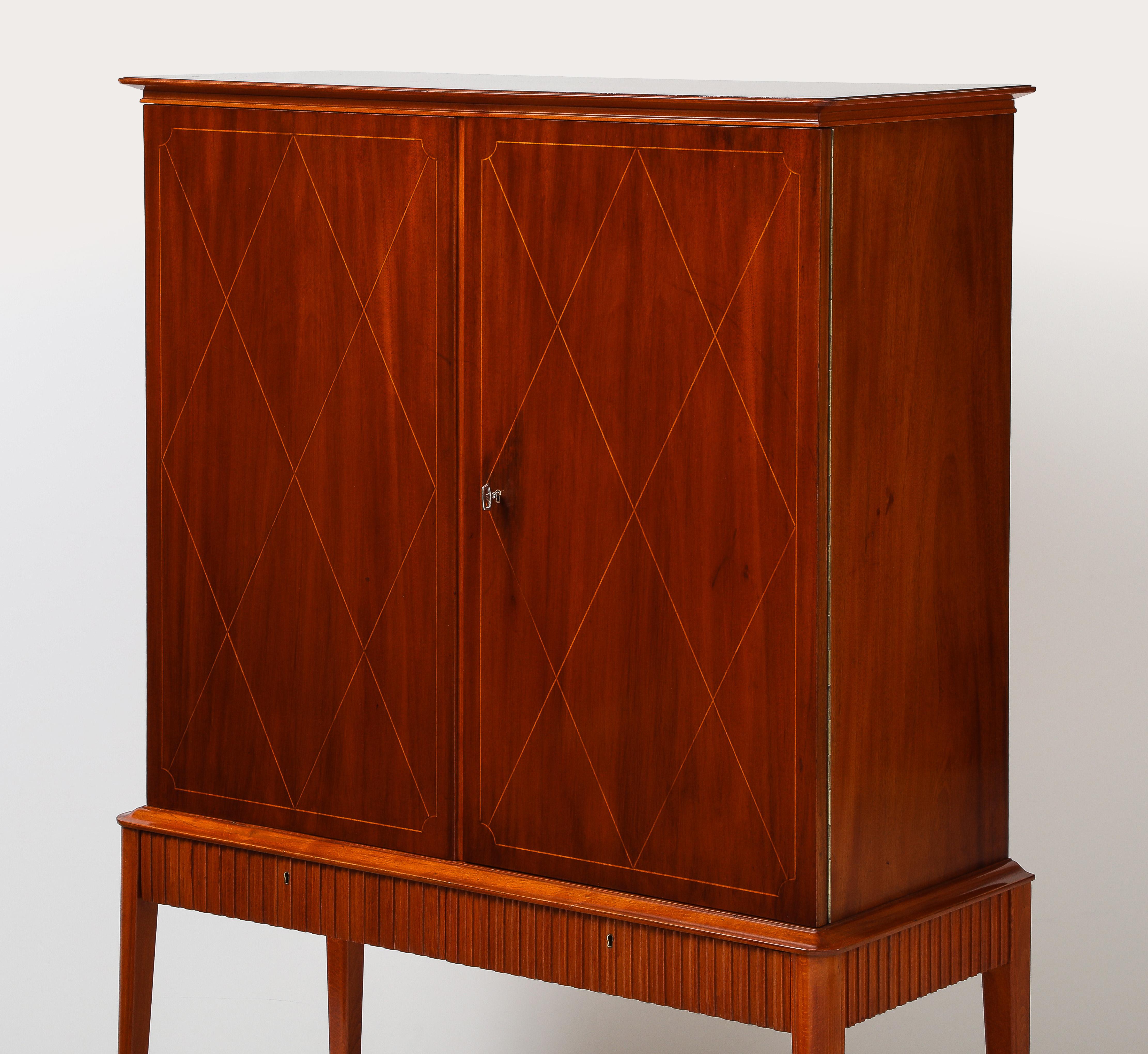 Armadio svedese SMF Svenska Möbelfabriken Bodafors in mogano con intarsi in legno di frutta, CIRCA anni '40. Il piano rettangolare sporgente con angoli arrotondati sovrasta due ante di armadietto con incastri a diamante in legno di frutta. La parte