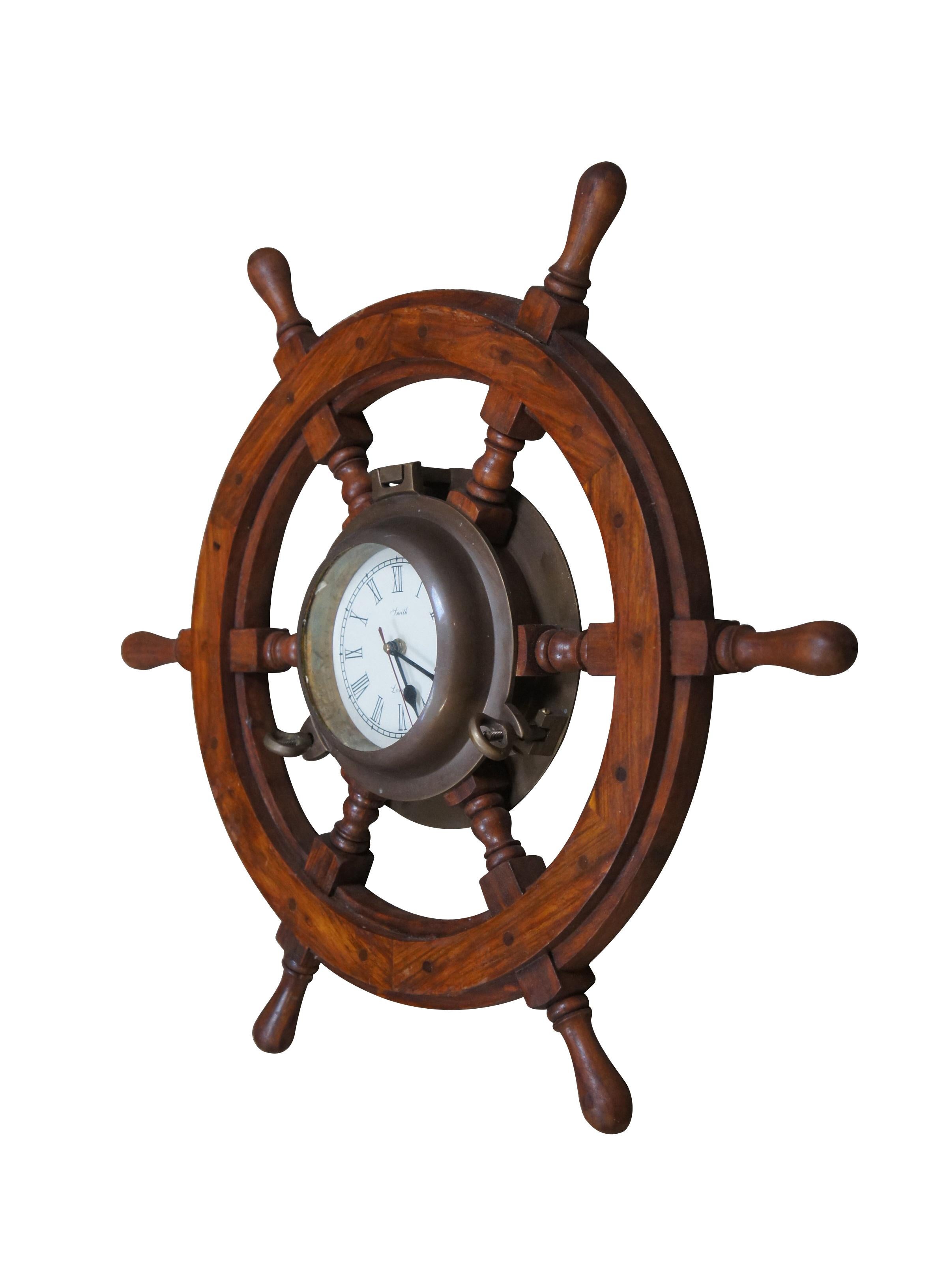 Late 20th century nautical wall clock in the shape of a wooden ship's wheel / helm, with the face framed in a brass porthole. White face with Roman numerals. Made in India. Prestige Quartz battery operated movement.

Dimensions:
24.5