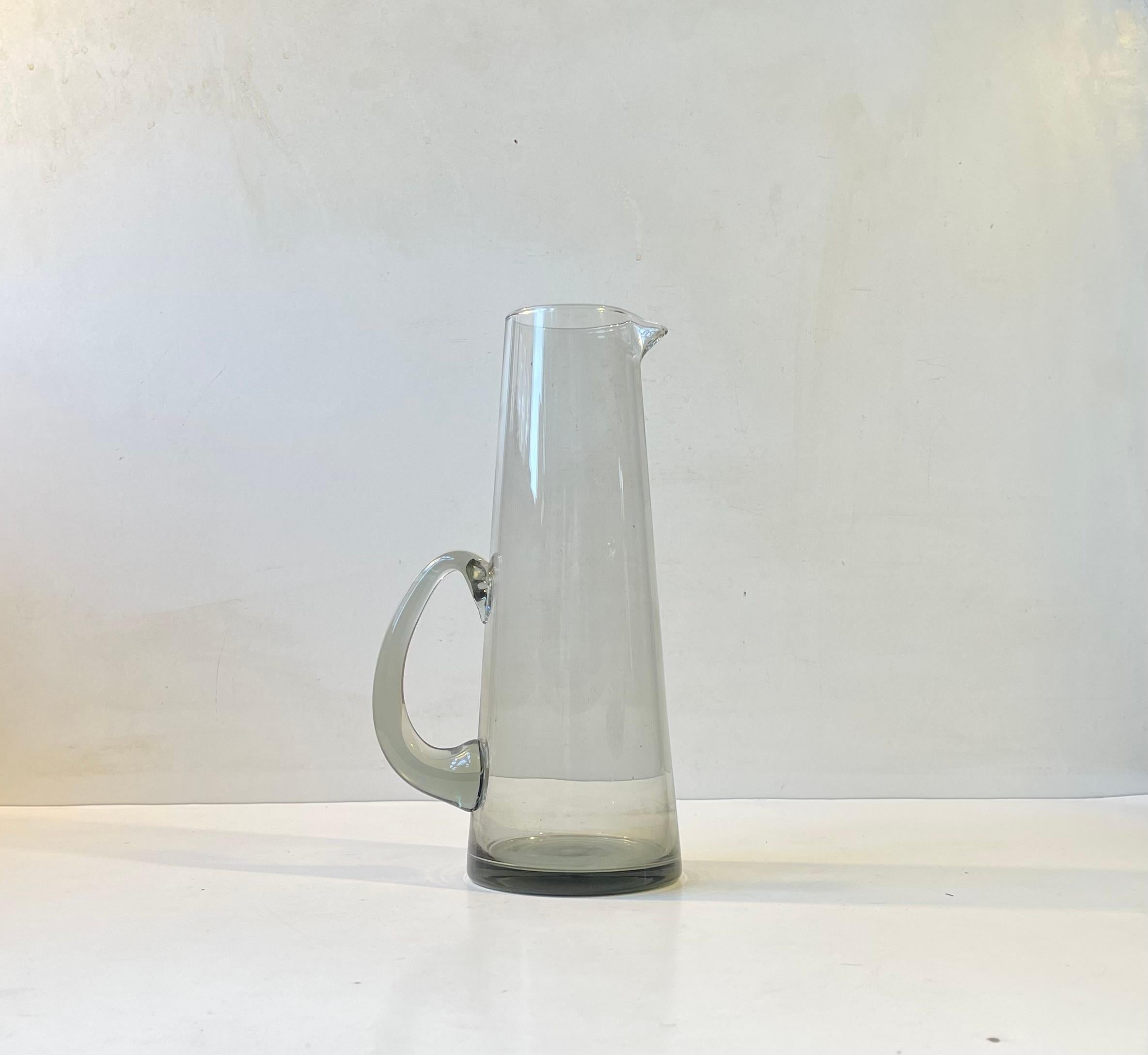 Elegant hand-blown pitcher in grey smoke glass designed by per Lütken circa 1960 and made Holmegaard in Denmark. Measurements: H: 25 cm, Diameter: 9.5 cm (base). Capacity: 0,7 liter.