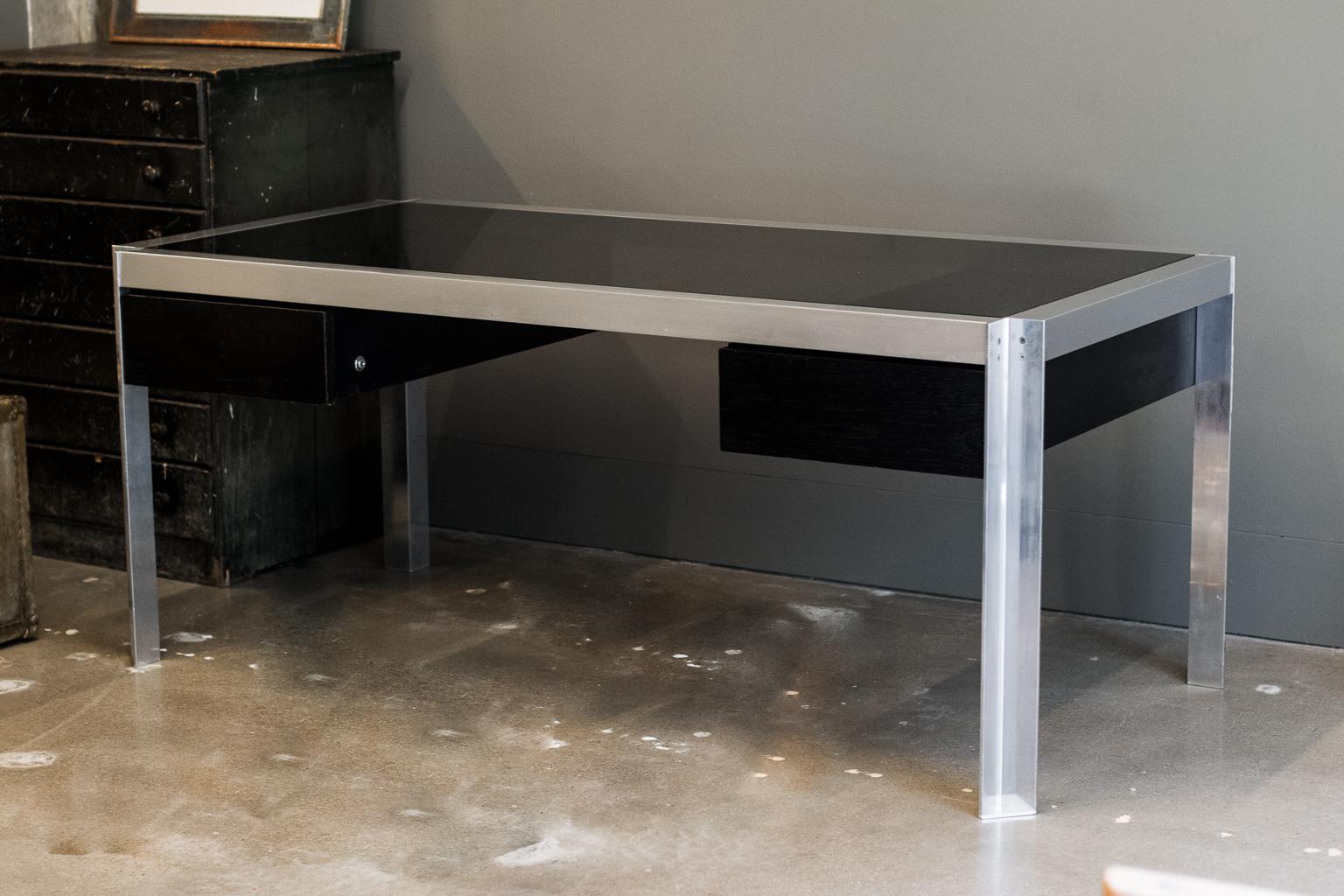 Inspired after meeting renowned architect and designer Le Corbusier, Georges Frydman founded his award-winning company E.F.A. in France in 1954. Executive desk with aluminum frame and dark stained wood drawer fronts, topped with smoked glass. France