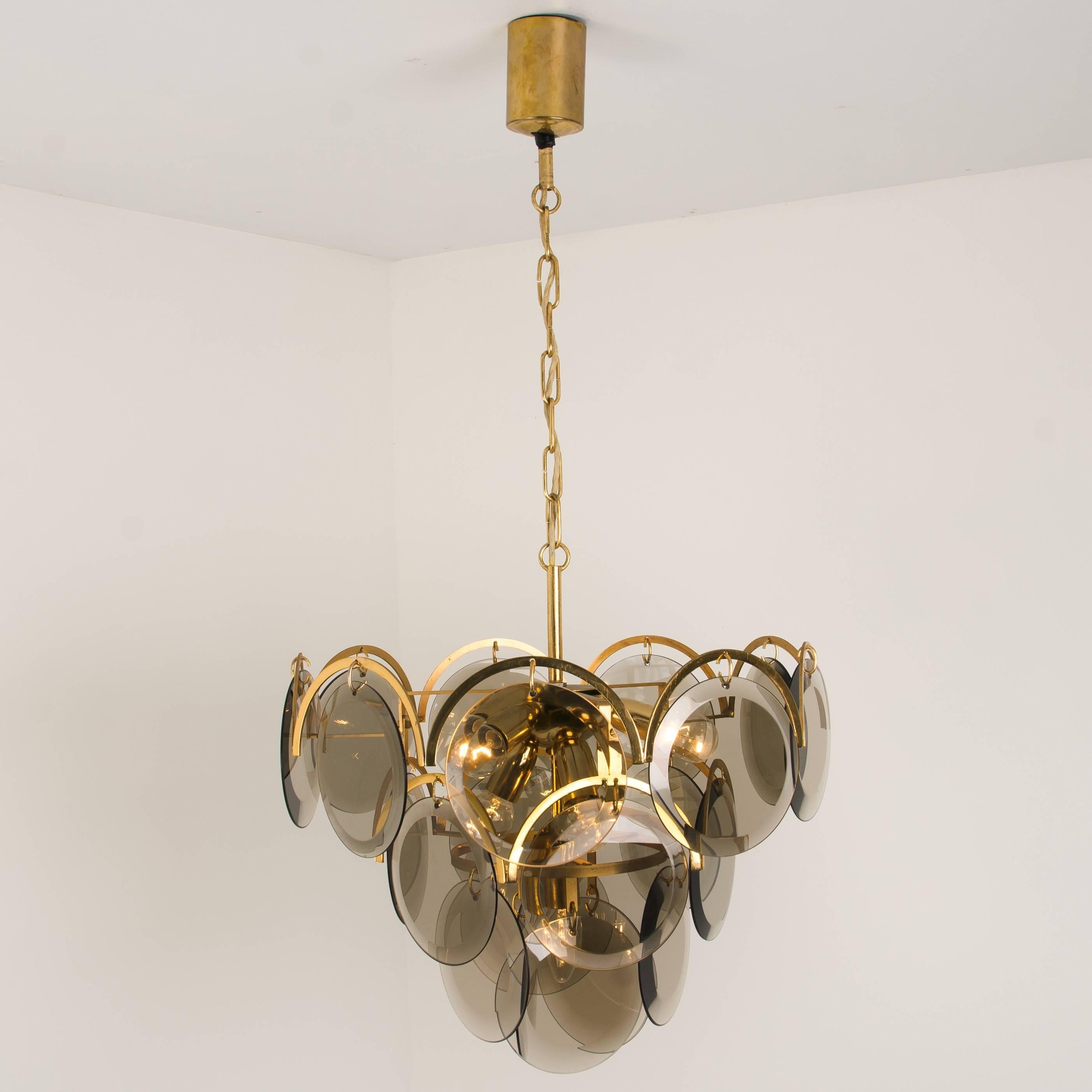 A gourgios four tiers hanging light fixture, attributed to Vistosi, Italy, manufactured in circa 1970 (late 1960s and early 1970s). With graduated tiers of smoked round facet chaped glass discs framed by half moon shaped brass. The chandelier is