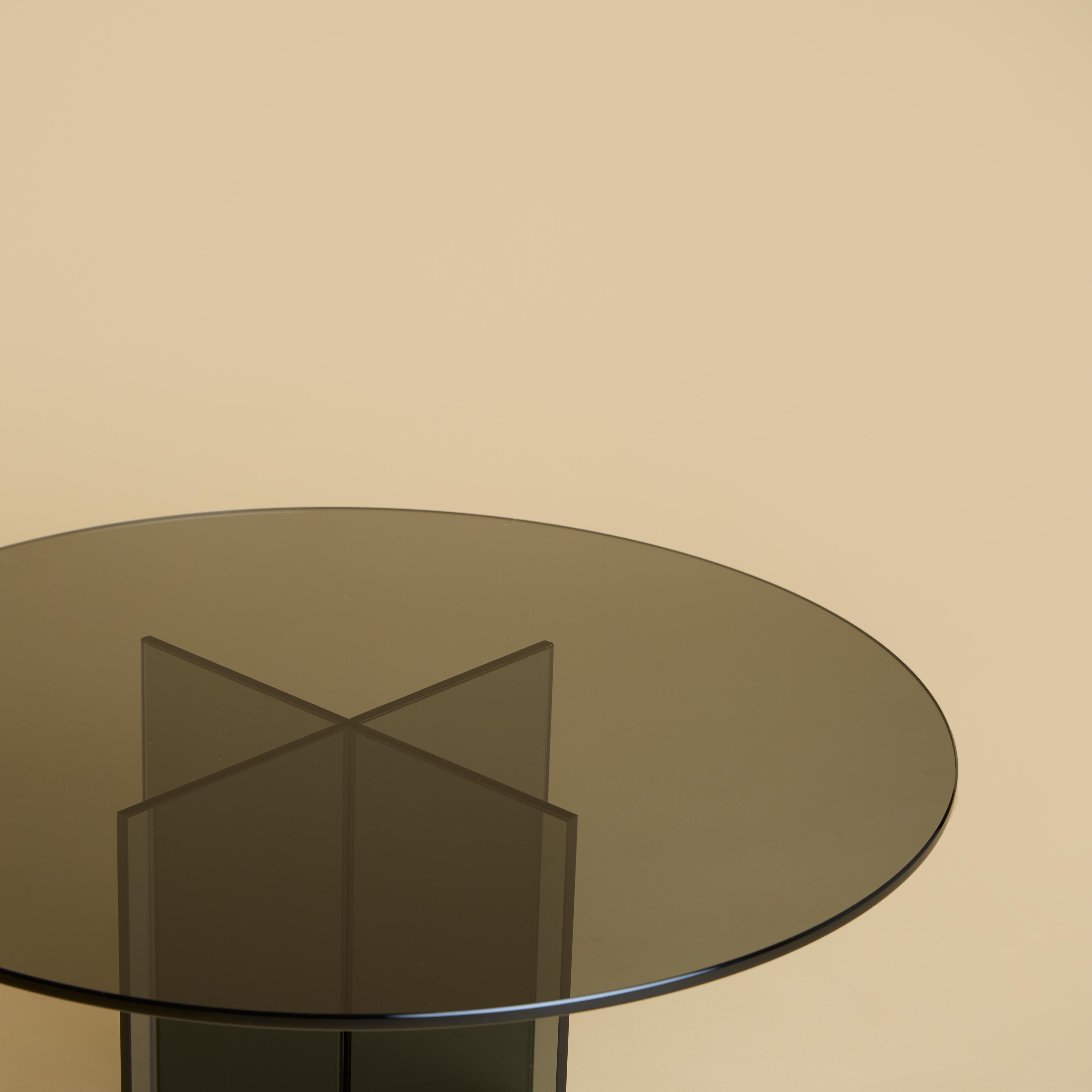 The coffee table Aka is made entirely of smoked glass. The top is circular and 60cm in diameter, while the base is obtained by gluing slightly bevelled 6mm thick slabs.
Coffee table made by grey smoked glass which combines easily with other trendy