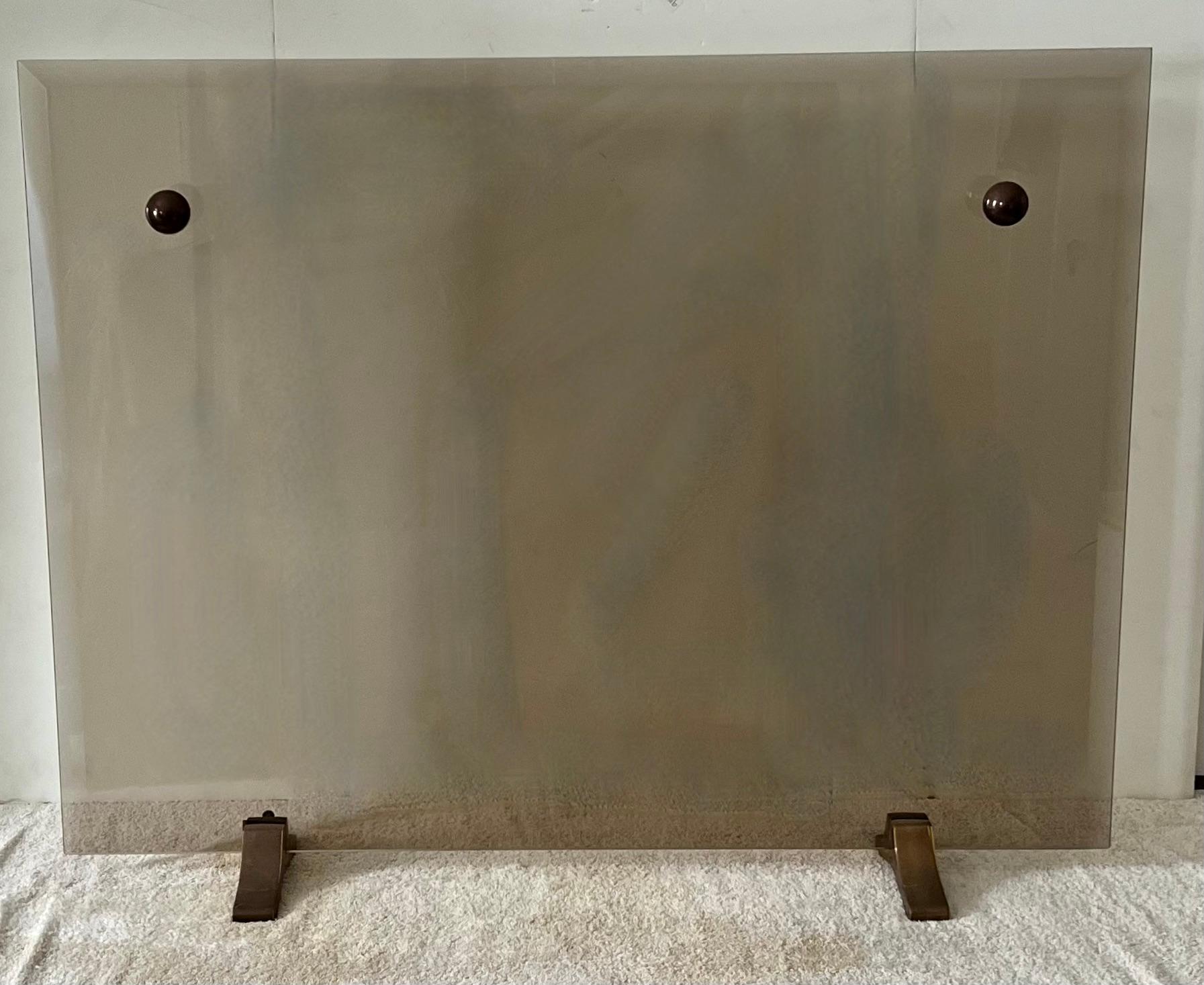 A smoked glass fireplace screen. The glass is beveled and is on panel supported by two bronze feet. the glass has two spherical knobs, which make moving the piece much easier than trying to pick up the entire piece of glass.

The simplicity is quite