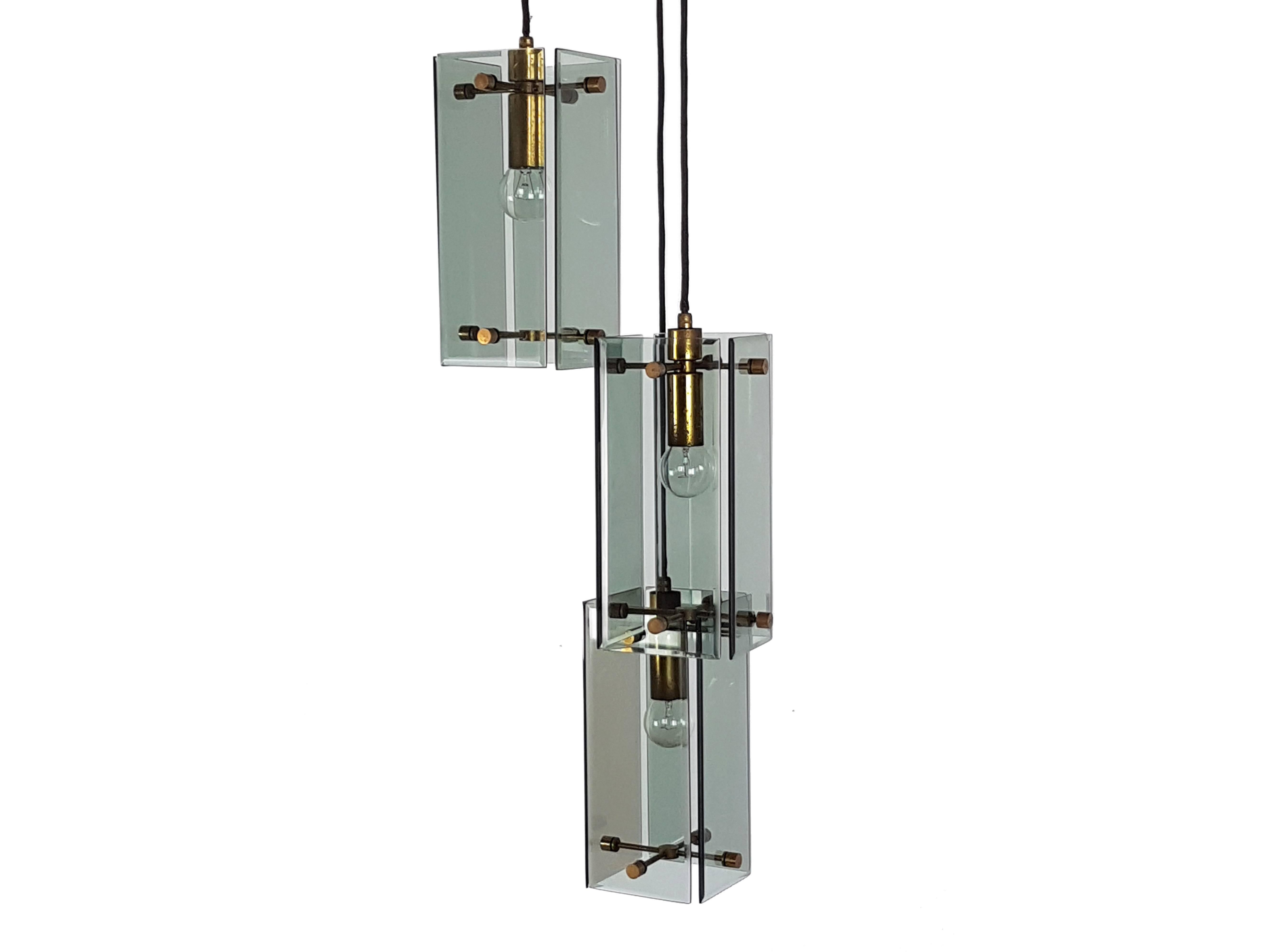This elegant lamp was produced in Italy, circa 1960s. It is composed by three-lights pendants at different adjustable heights. Each element is made from a brass structure with four smoked glass shades. A wooden and golden metal ceiling supports