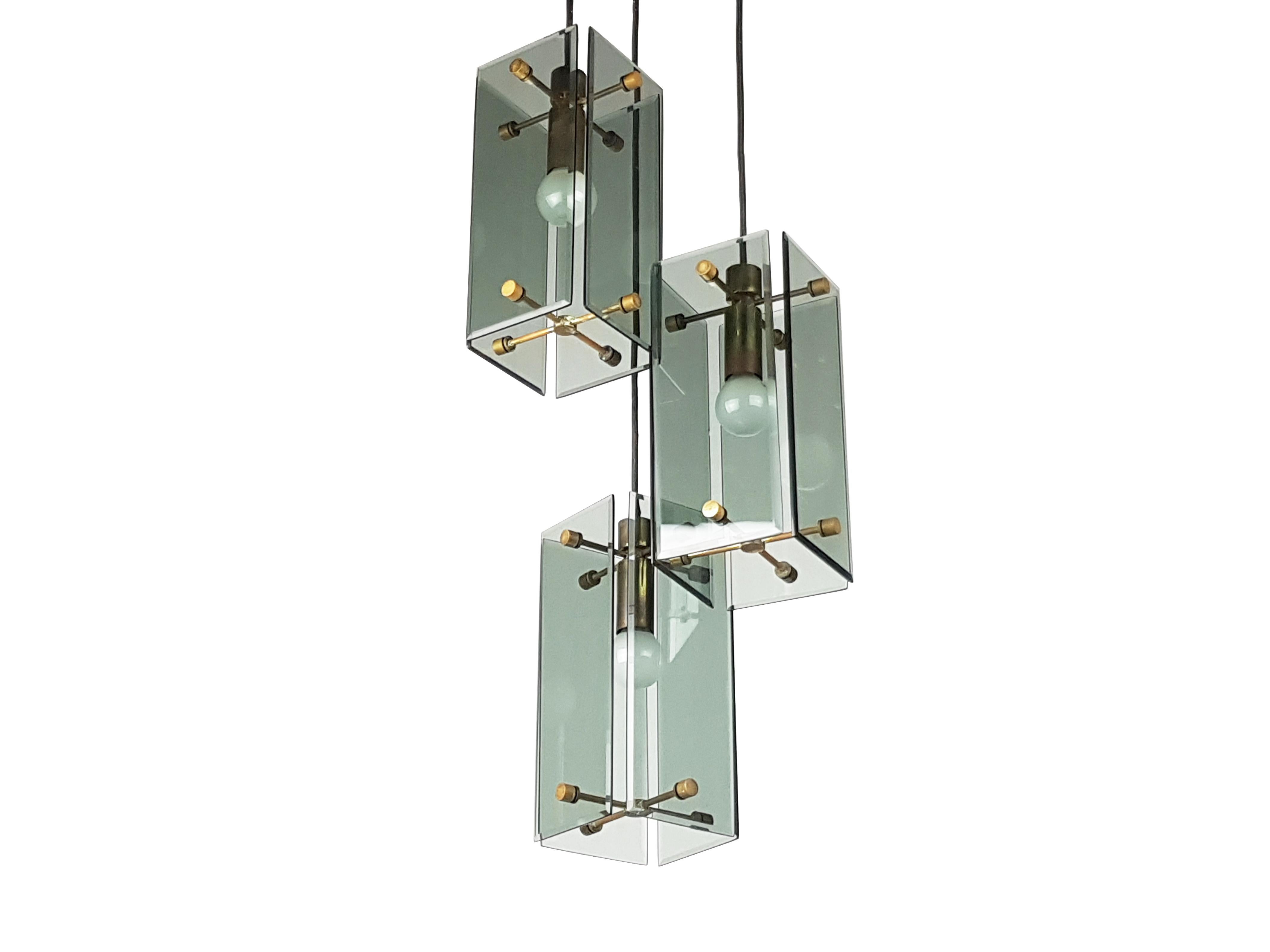 Cette lampe élégante a été produite en Italie dans les années 1960. Il est composé de pendentifs à 3 lumières à différentes hauteurs réglables. Chaque élément est constitué d'une structure en laiton avec 4 abat-jour en verre fumé. Un plafond en bois