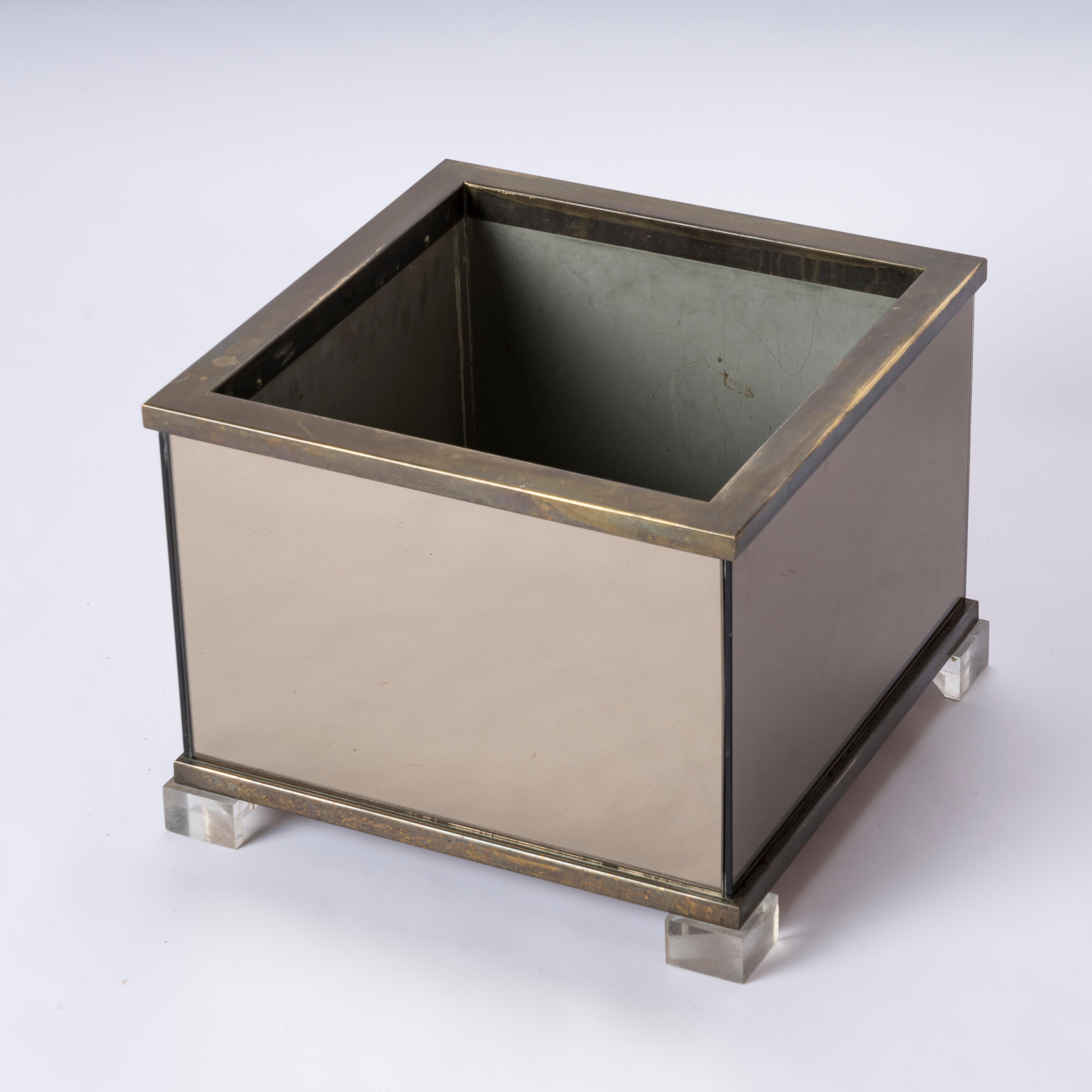 Sleek 1970's planter with smoked mirror pannells, brass trimmings and lucite feet attributed to Maison Jansen. 
In good vintage condition. Some scratches on lucite feet. Patina on brass.
This planter will ship from France and can be returned to
