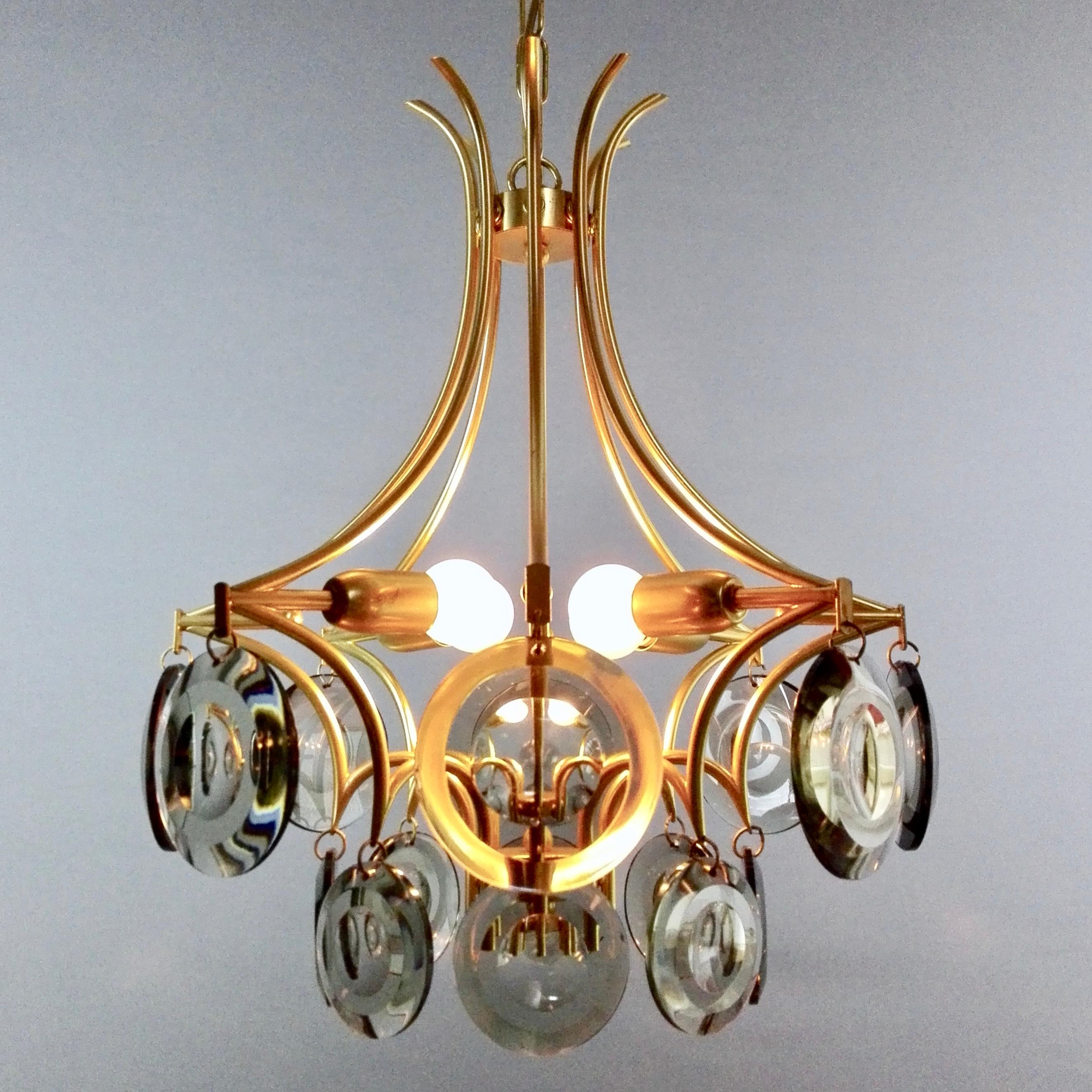 Very particular four-light Italian 1970s chandelier in the style of Vistosi. The fixture has a gilded metal structure composed of eight arms that descend widening from the top. 
Note the very creative way in which the lamp holders are alternately