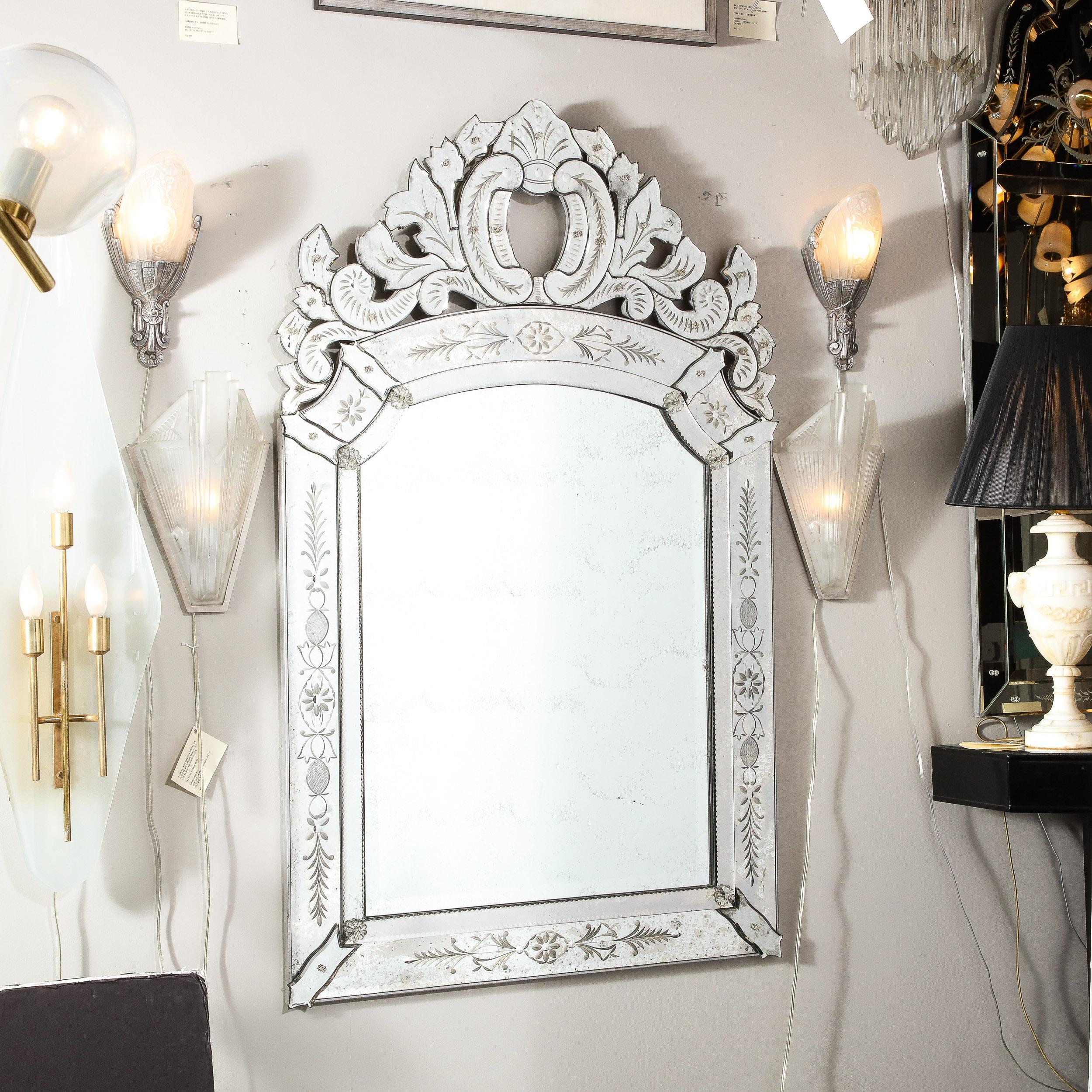 This elegant Mid-Century Modern Venetian mirror was realized in France circa 1950. It offers a subtly smoked and antiqued perimeter- with a plain mirror center- that features rectangular panels on each side and on bottom with notched mirrored