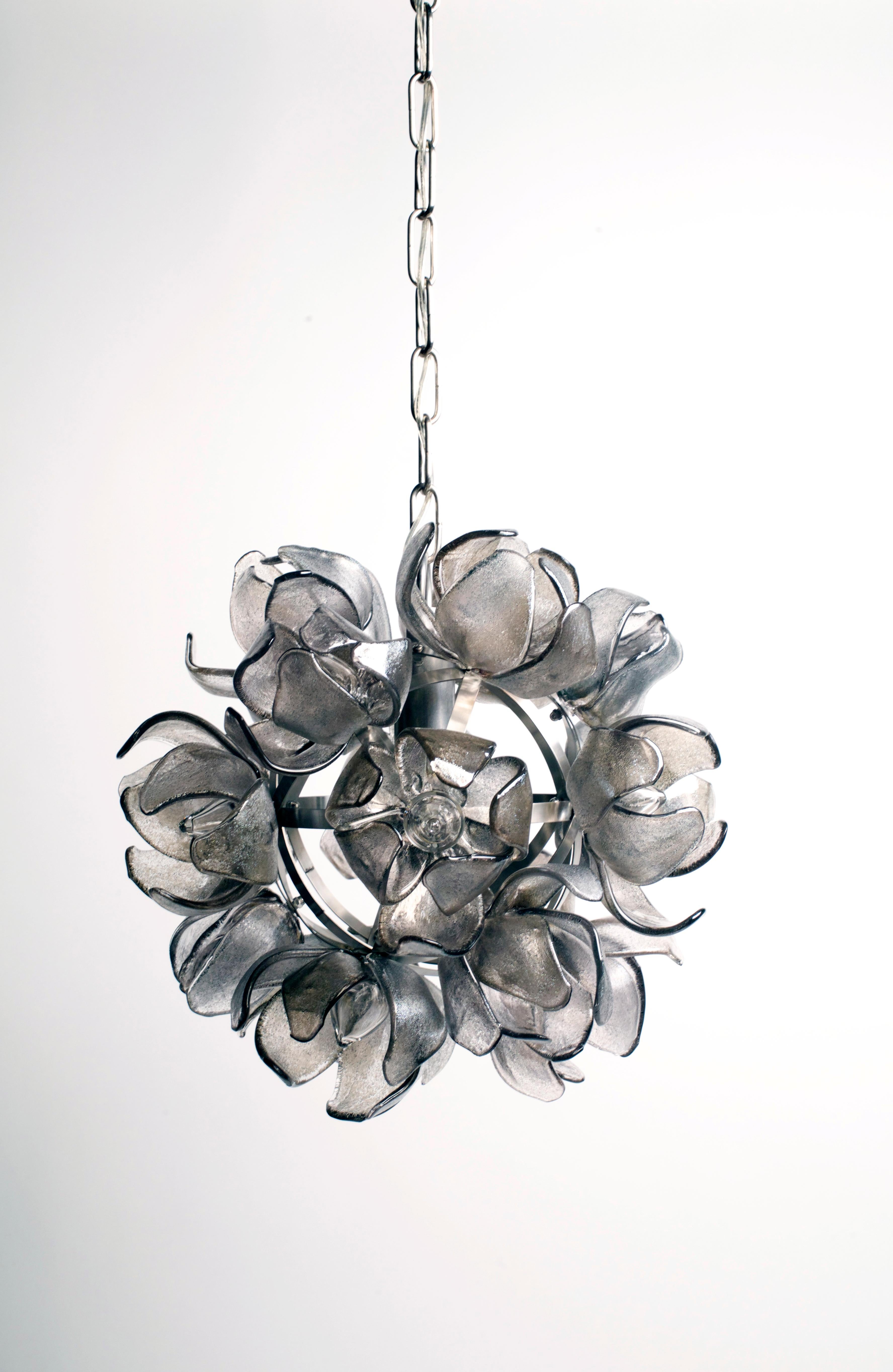 This smokey grey glass Magnolia Chandelier on a stainless steel structure by Elizabeth Lyons is one of the round floral series. A total of 18 glass magnolias adorn a stainless steel structure to create a gorgeous 16