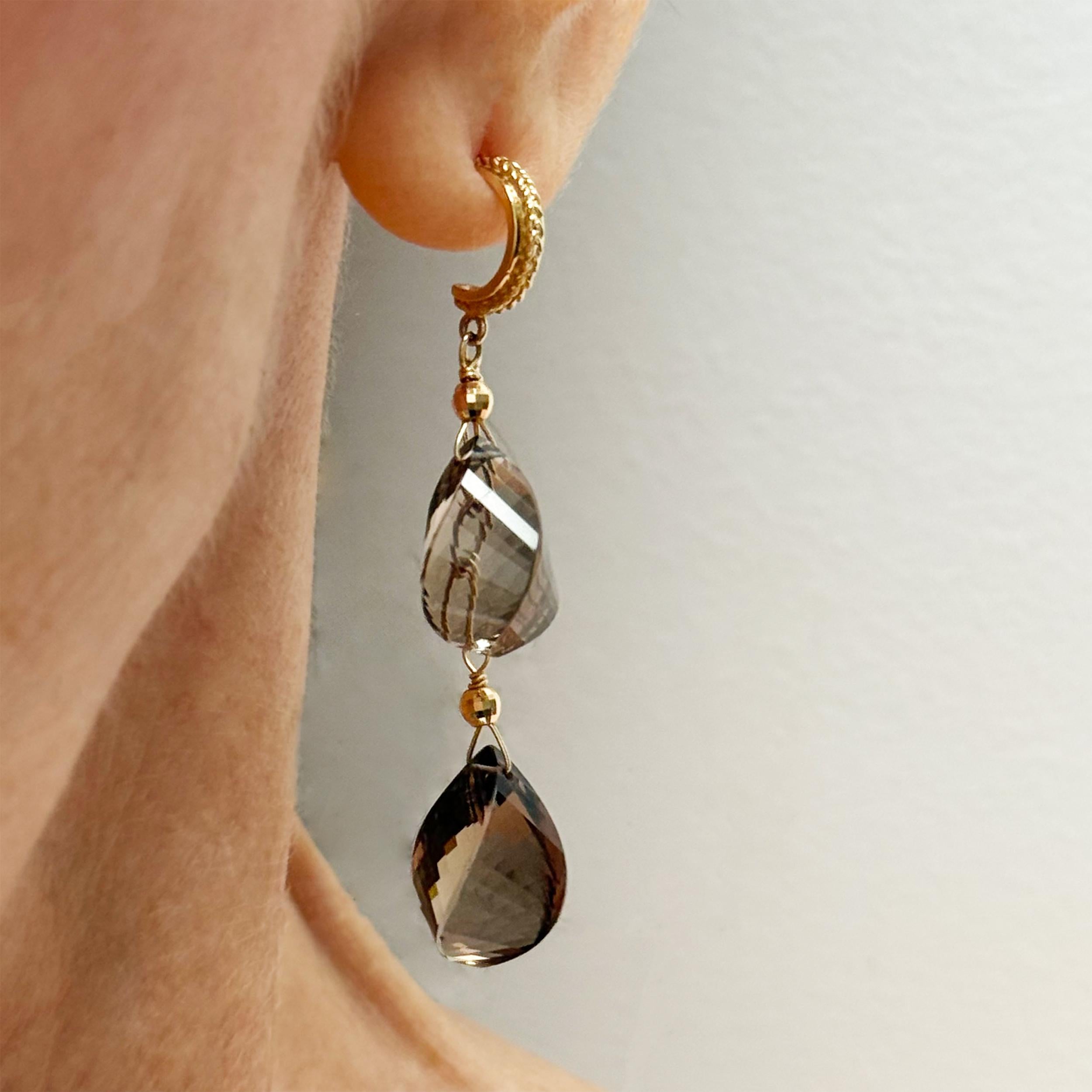 Description
Des gouttes de quartz fumé de taille unique, couronnées de perles d'or jaune 14k facettées, se balancent élégamment sur de fines chaînes suspendues à des poteaux demi-coeur texturés. Une gracieuse fusion de mouvement, de profondeur et de