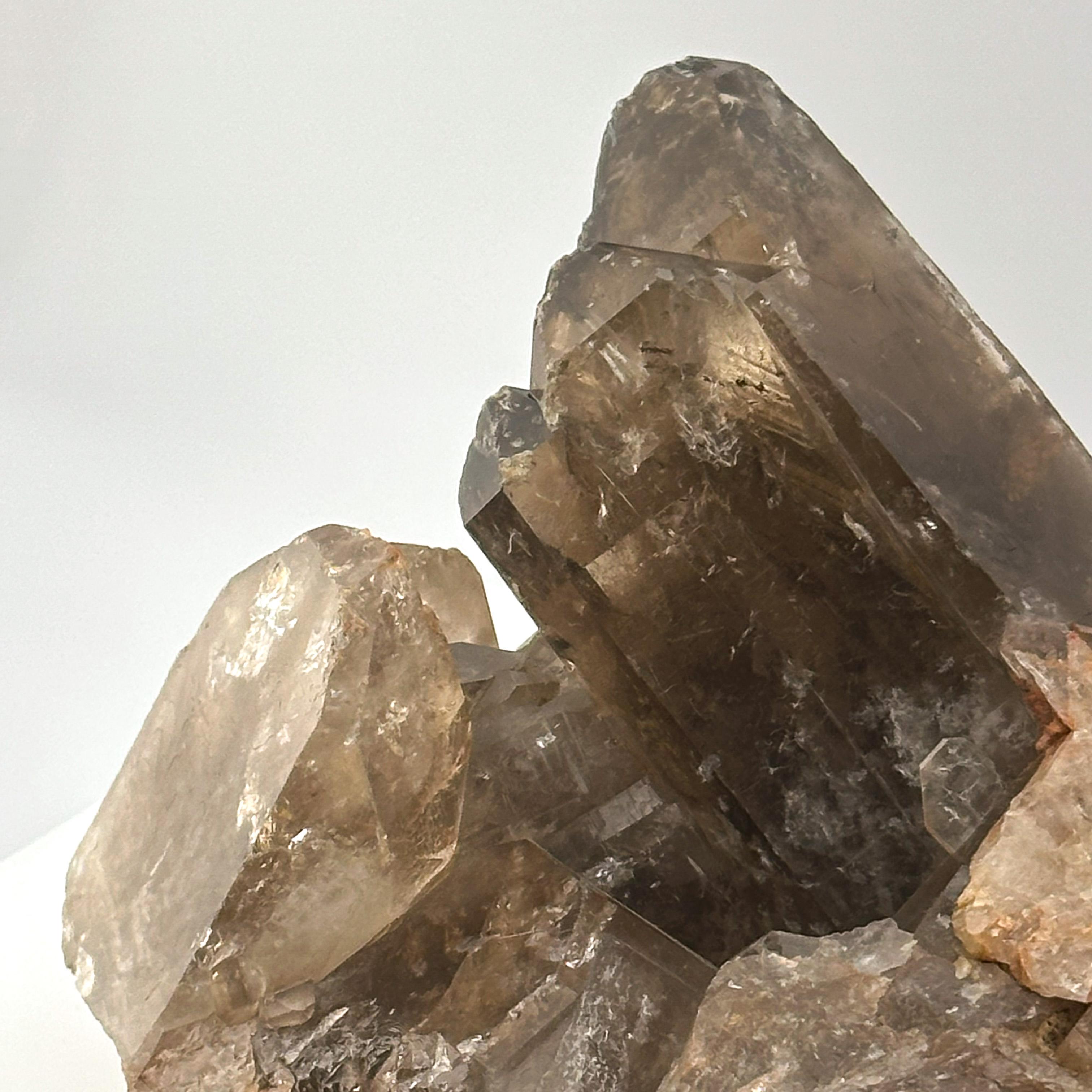 A visually dynamic smoky quartz crystal cluster, showcasing multiple sharply terminated points growing from a natural quartz matrix. 

This raw mineral specimen measures approximately 15 cm wide, 10 cm deep, and 9 cm tall. The quartz ranges from