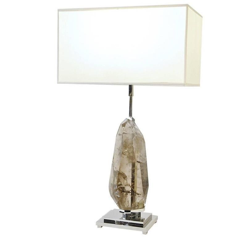 A marvellous one-of-a-kind piece of hand-cut, light-colored smokey quartz rests mounted on a handcrafted base of nickel-plated brass, constituting the body of this lamp, which is paired with a creamy white colored rectangular shade. This natural