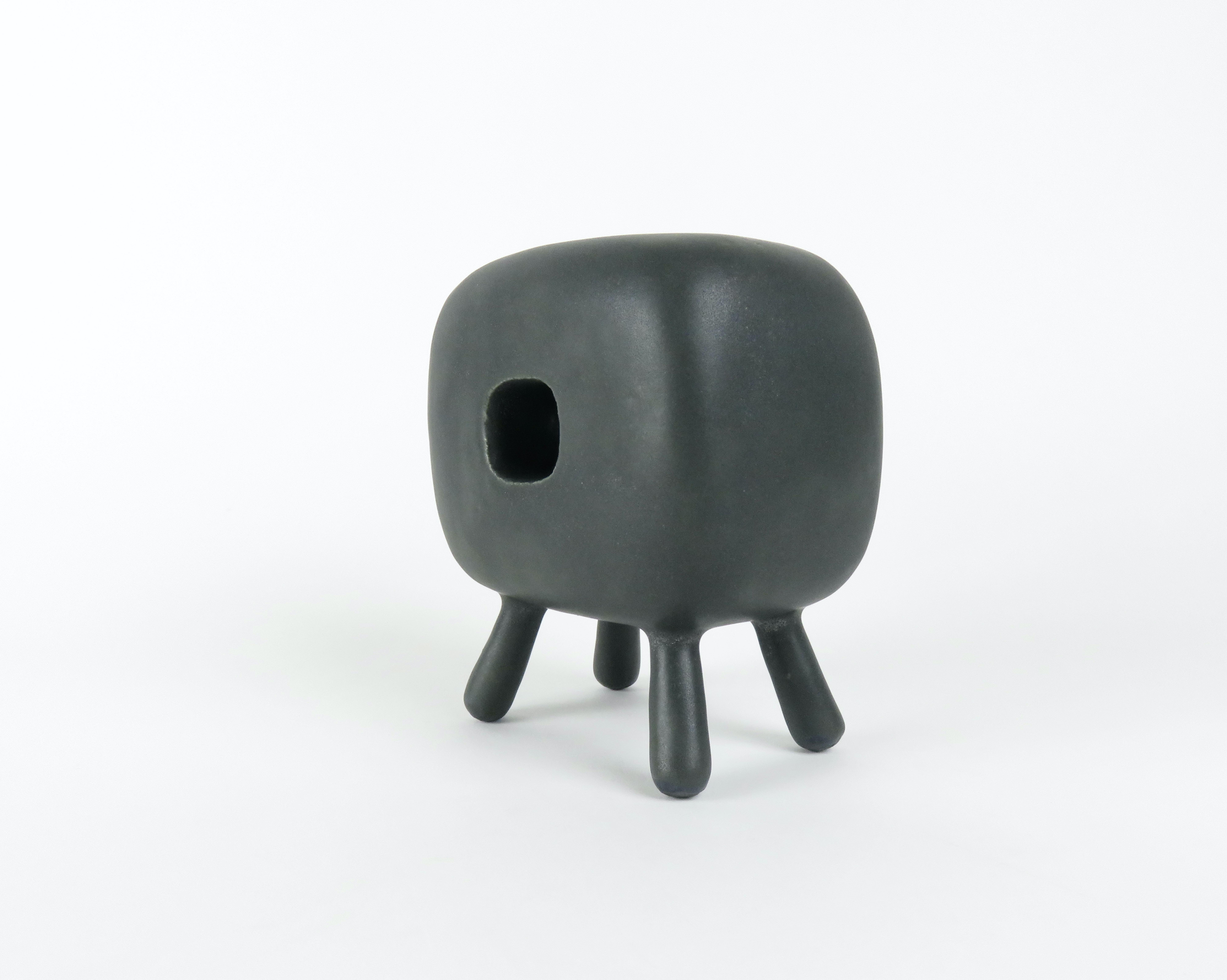 This small hand built rectangular ceramic sculpture with square opening on 4 Legs is part of the Artist's ongoing series of Modern Totems. Starting with a dark brown clay body, the piece is glazed in a creamy thick matte black. The small cube on
