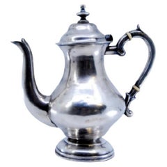 Caffettiera d
argento liscia con un pomello sul coperchio e appoggiata su una base rotonda