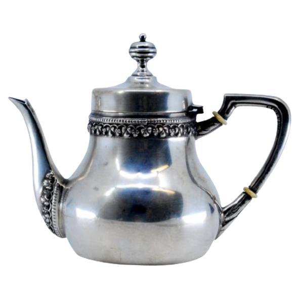 Cafetière en argent lisse avec garniture sur le bord et le bec, bouton sur le couvercle.