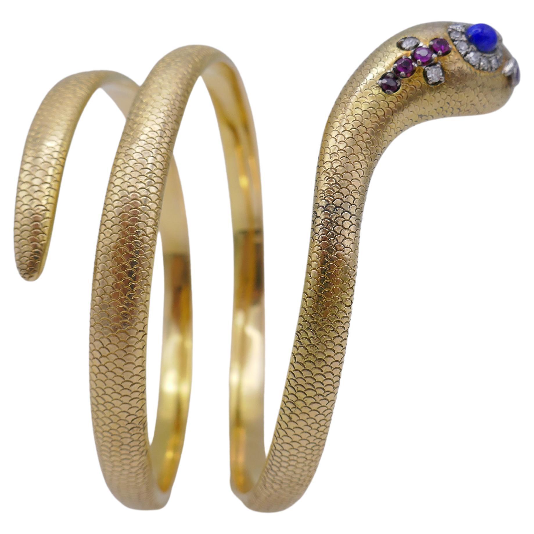 Ein exquisites Schlangenarmband aus Gold mit Edelsteinen.
Das Armband ist in Form einer aufsteigenden Schlange gestaltet, deren Kopf mit Lapis, Diamant, Rubin und Smaragd verziert ist. Die 