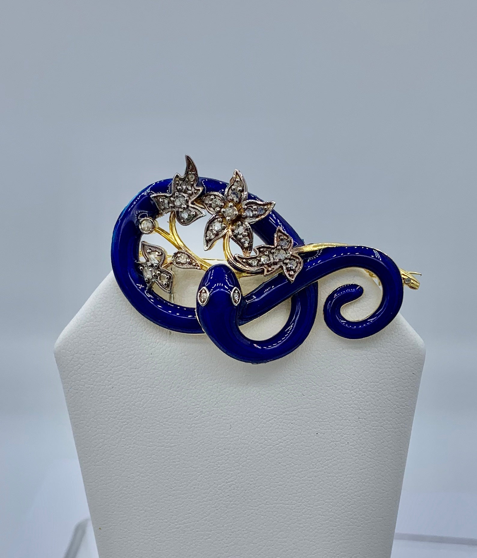 THIS IS A STUNNING SNAKE BROOCH IN THE FORM OF A SNAKE HOLDING DIAMOND ENCRUSTED FLOWERS IN ITS MOUTH.   THE SNAKE IS ADORNED WITH THE MOST STUNNING BASSE-TAILLE ROYAL BLUE ENAMEL.
And snake jewelry is all the rage today.  In the Victorian era the