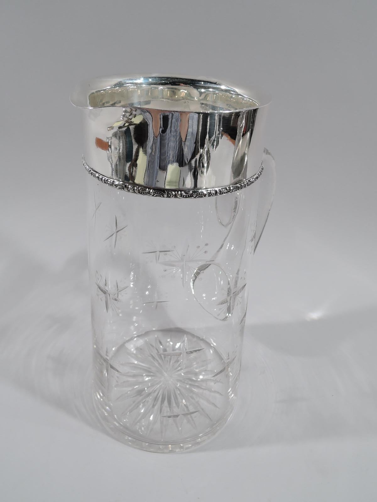 American Art Deco sterling silver and glass bar pitcher, circa 1920. Upward tapering body with looping scroll handle. Star cut to underside; on body cut crosses sprouting acid-etched beaded stalks. Sterling silver collar with tooled scroll and