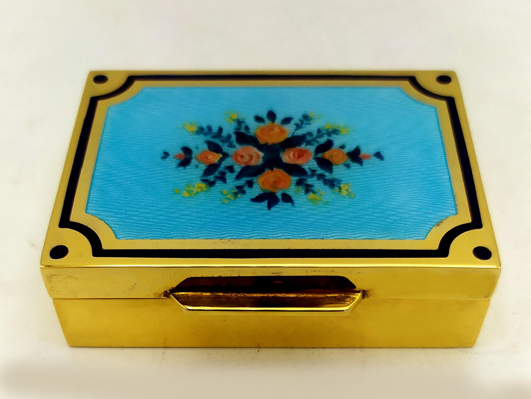 Tabacchiera rettangolare da tavolo in argento 925/1000 placcato oro con smalti traslucidi cotti a guillochè e miniatura floreale dipinta a mano; asta esterna blu. Stile Art Nouveau dei primi anni del 1900. Misure cm. 5 x 6,8 x 2. Peso gr. 166.